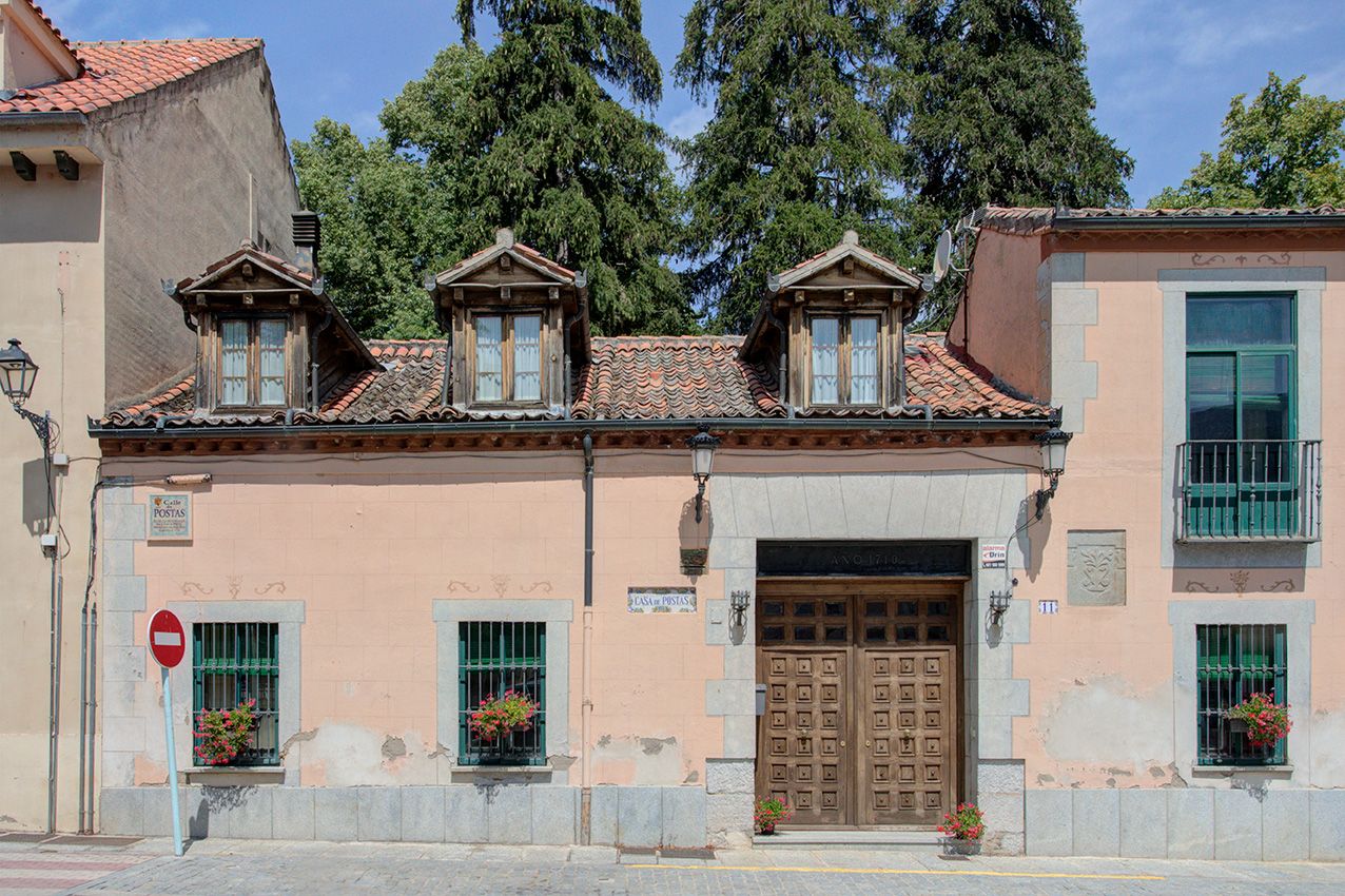 Historic pink Spanish building with dormer windows, wooden door, flower boxes, and tiled roof surrounded by trees.