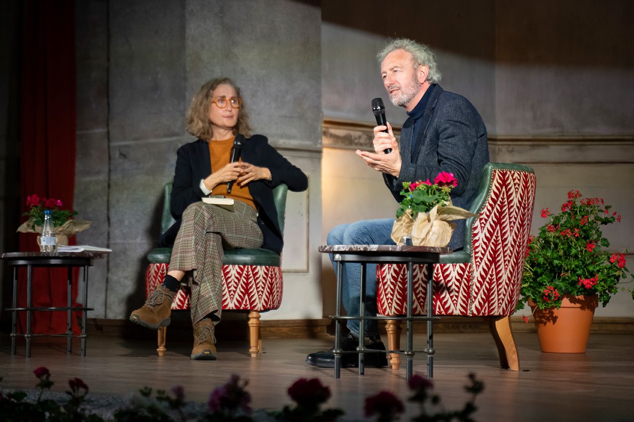 Two people seated in chairs on stage during a talk at La Granja en Flor event.