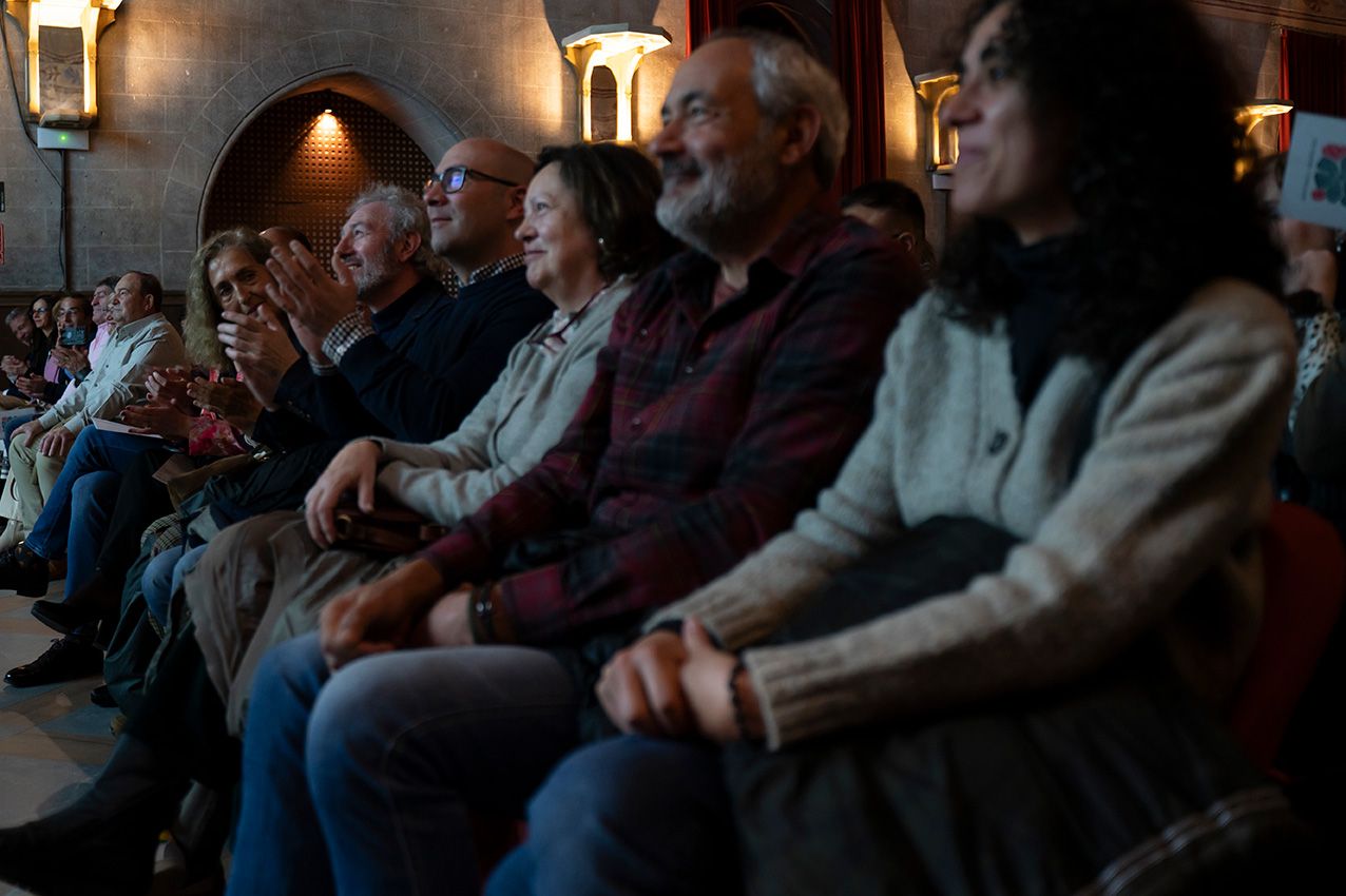 Smiling audience members seated in red chairs enjoying a live performance in an elegant venue.