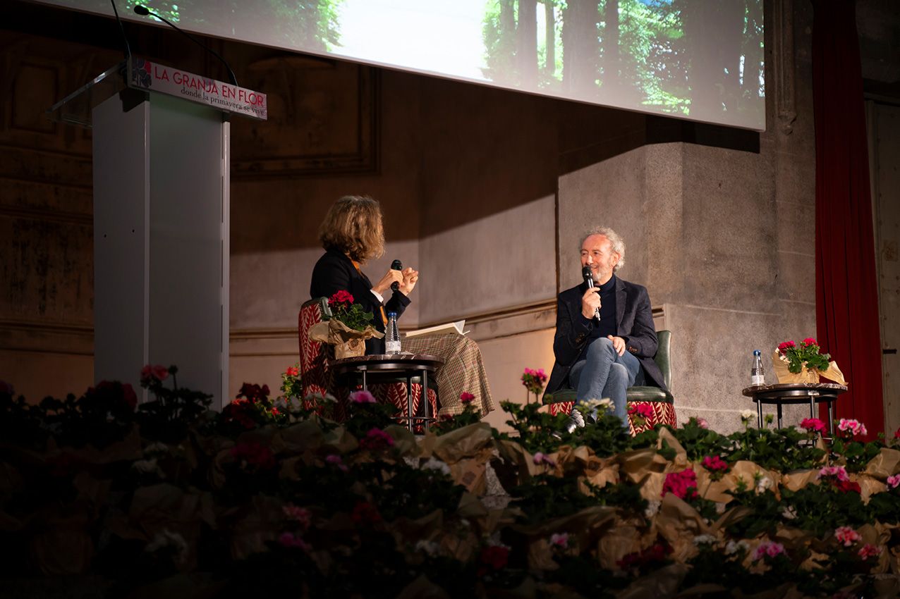 Two speakers in conversation on flower-decorated stage during garden art presentation event.