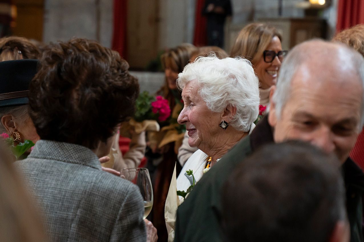 Senior woman with white hair laughing joyfully among guests at a social gathering.