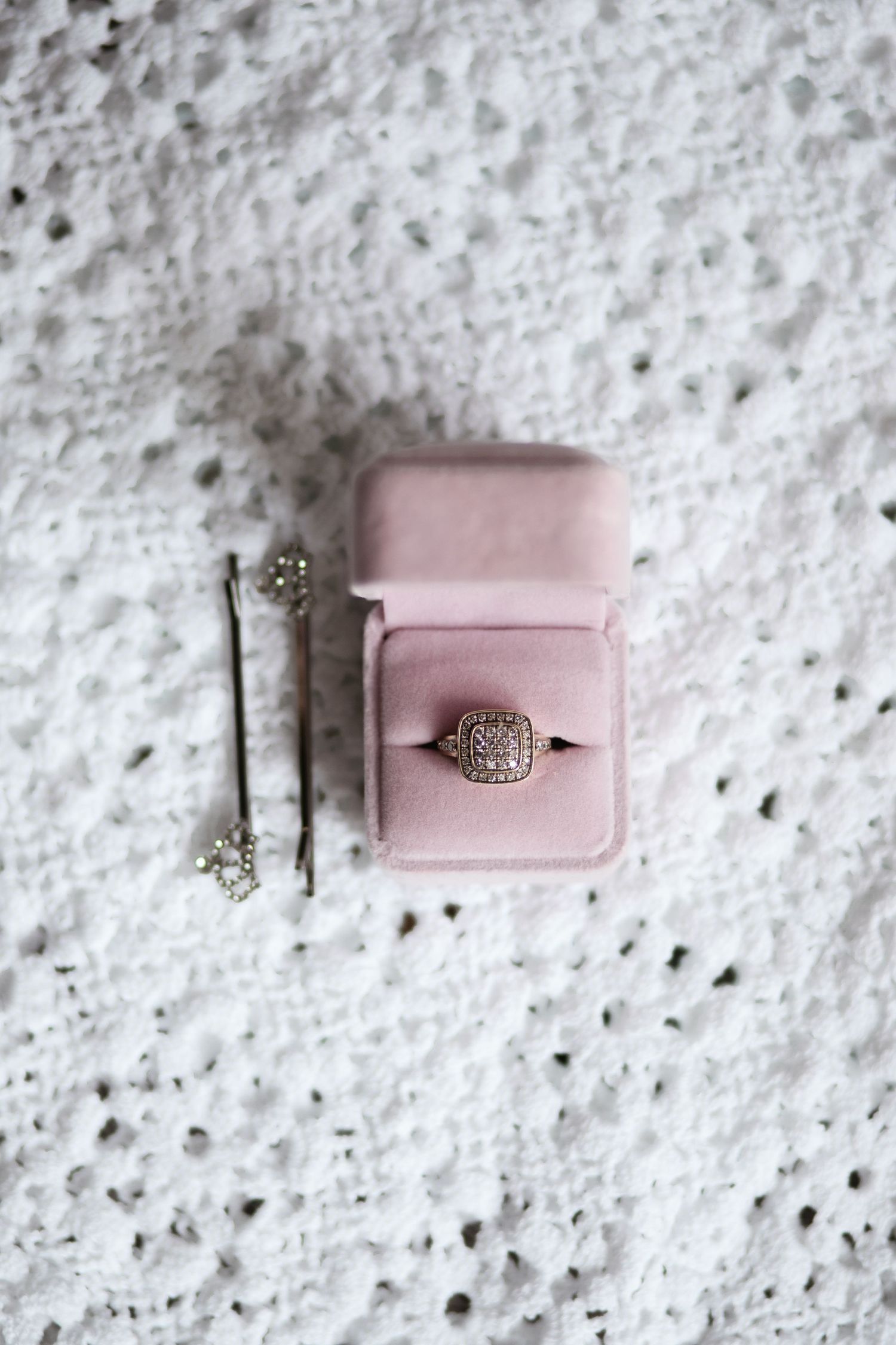 Flat lay of wedding ring and hair pins over white lace in Miami