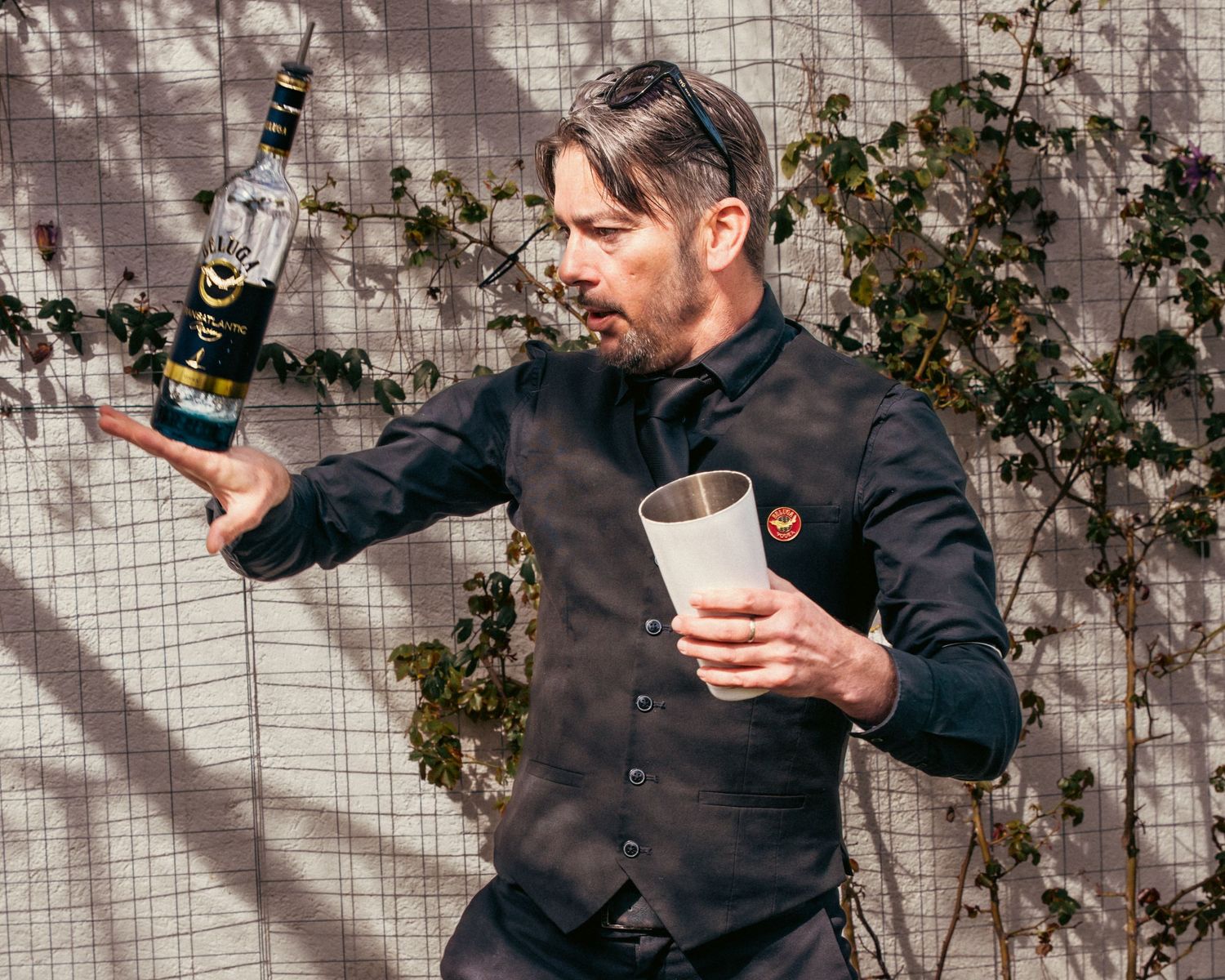 Person pouring drinks at an outdoor event with ivy-covered wall in background.