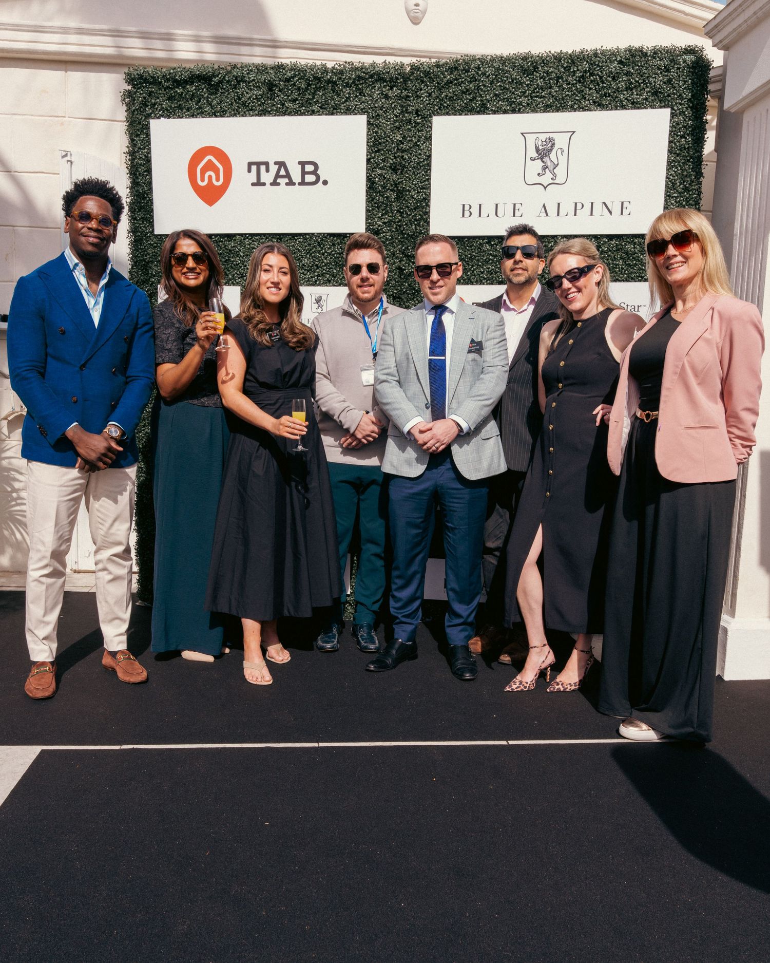 Group photo of event attendees standing in front of a branded backdrop wall.