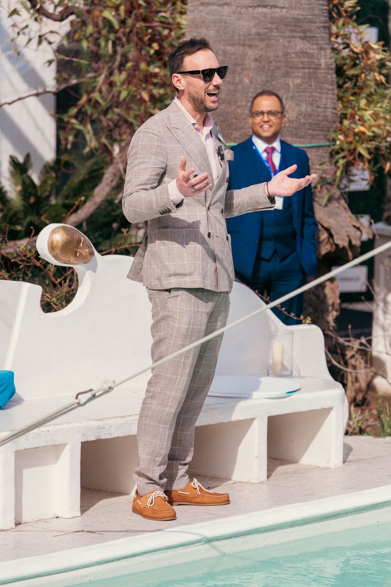 People in formal attire gesturing while standing near a pool at an outdoor venue.