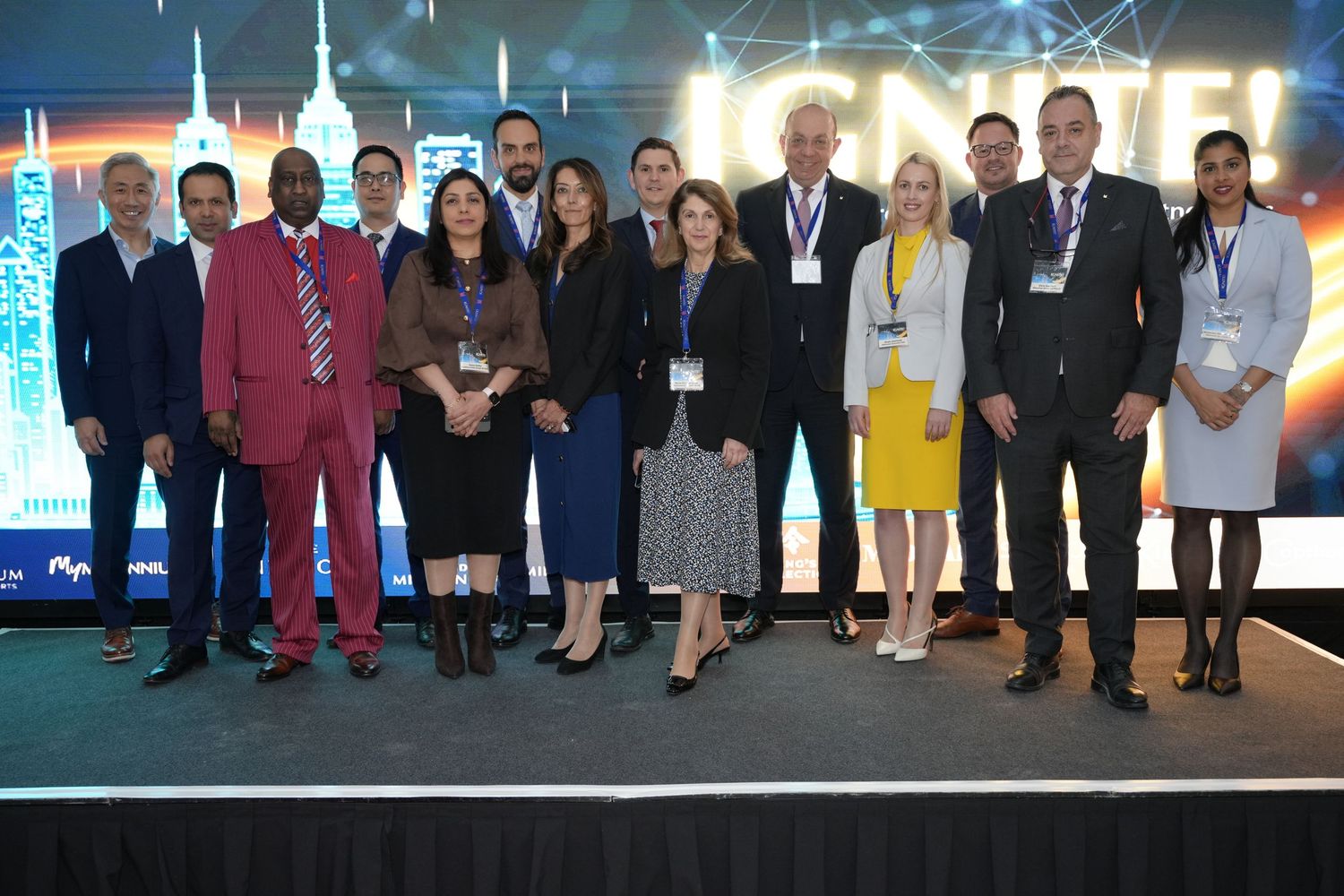 Group of professionals posing together at a corporate conference event with colorful stage backdrop.