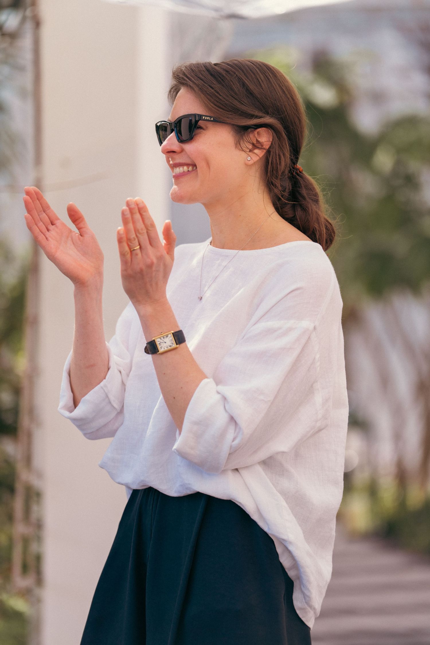 A person in a white top and dark skirt claps enthusiastically at an outdoor event.