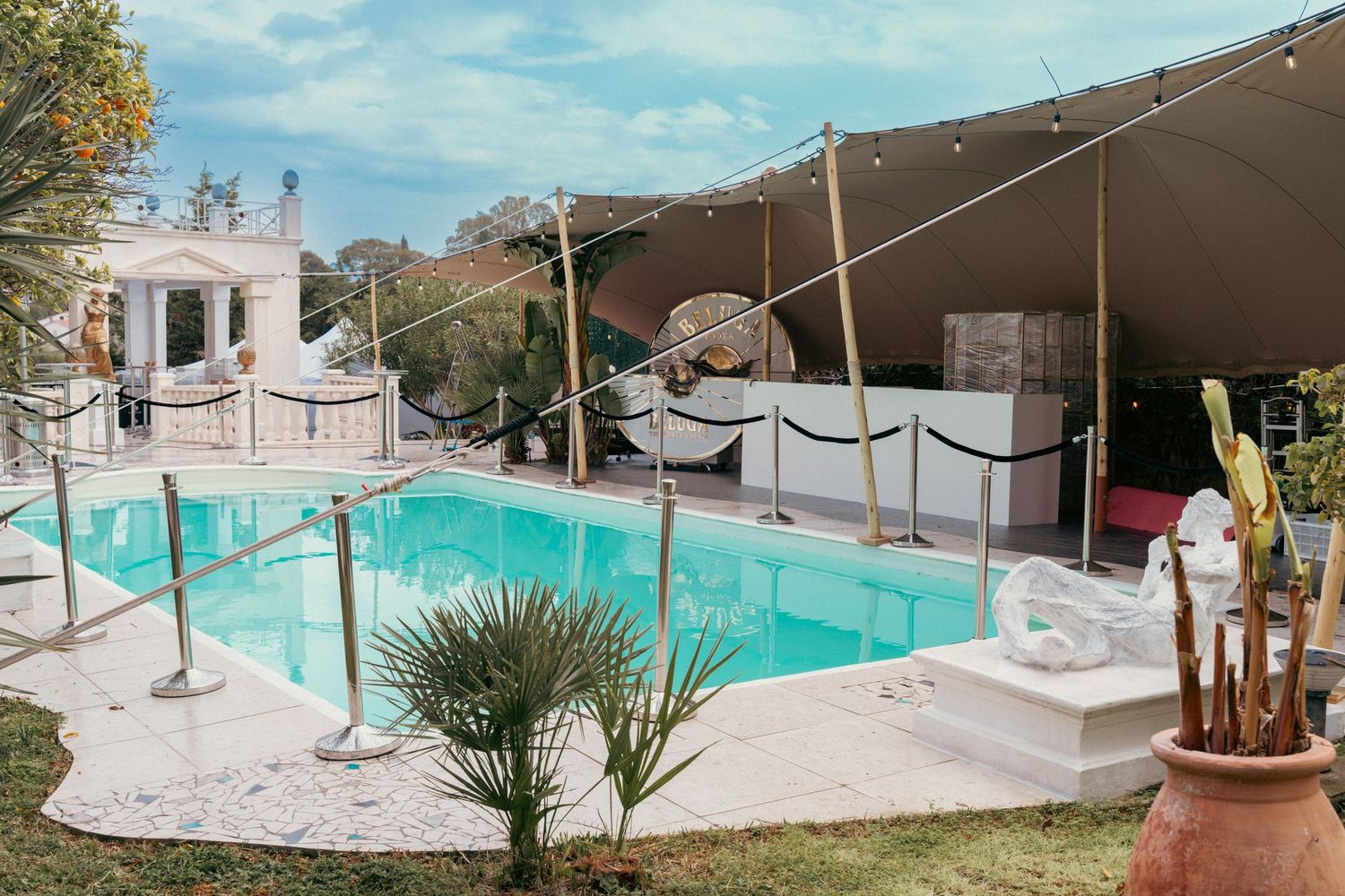 Outdoor pool area with white fencing and palm trees under blue sky.