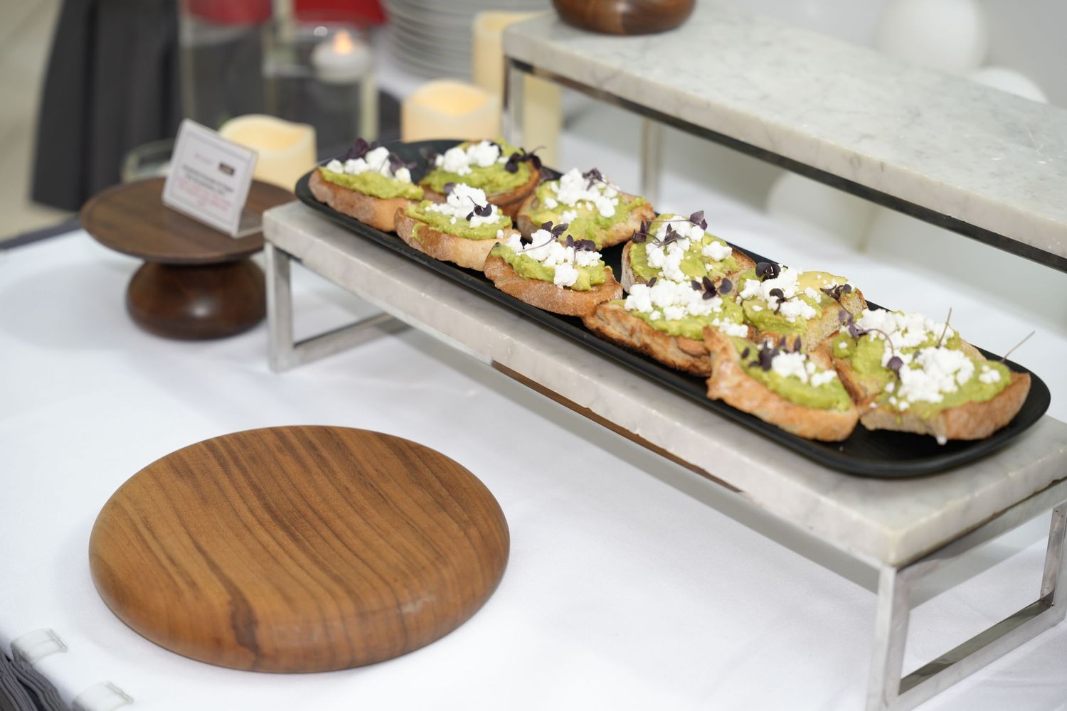 Elegant bruschetta topped with avocado, goat cheese, and olives displayed on a sleek serving platter at a catered event.