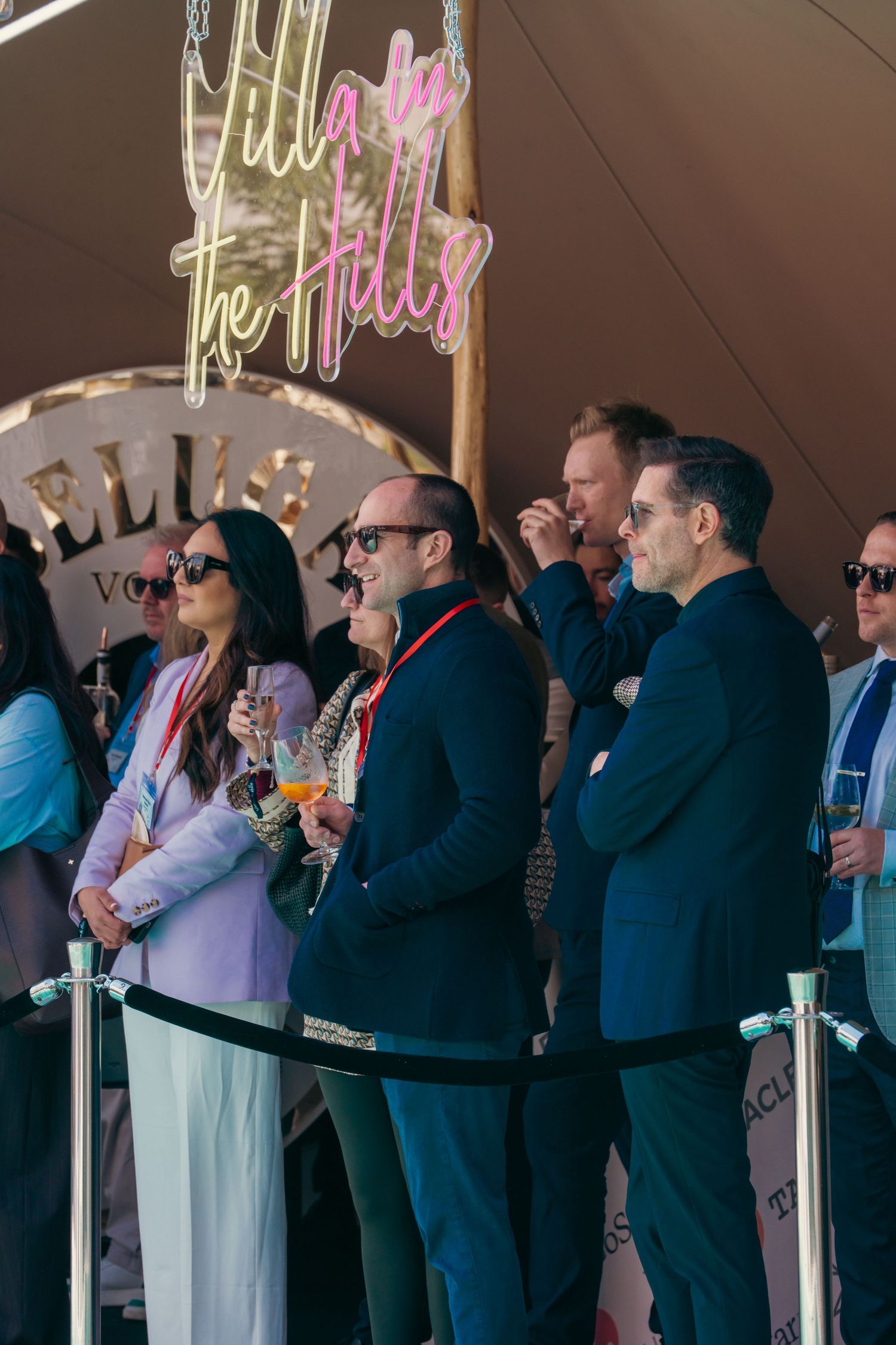 Conference attendees standing in rows under covered area with neon signage visible.