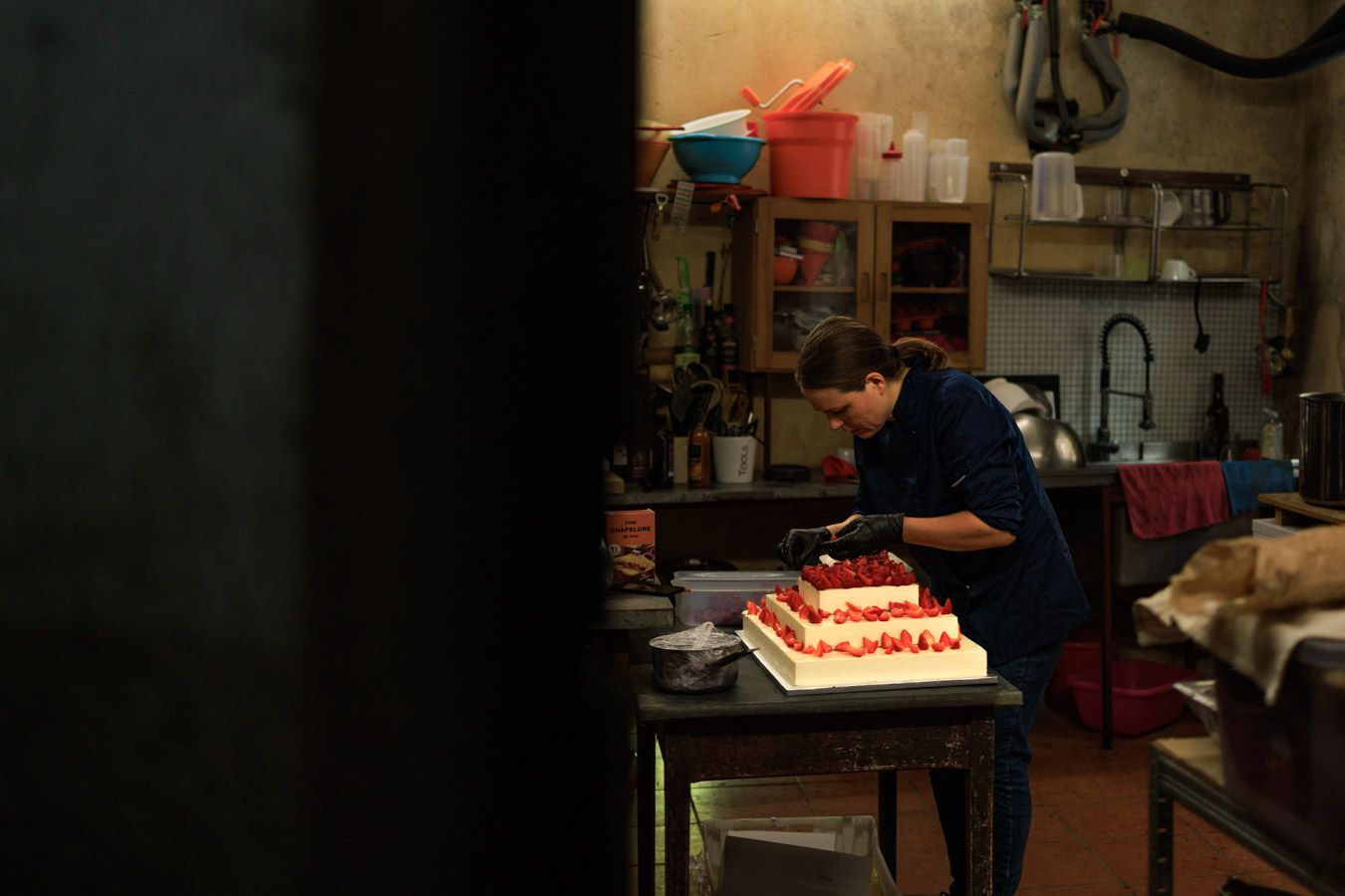 Cheffe pâtissière dans une cuisine d'un domaine en train de monter un gâteau trois étages aux fruits rouges.