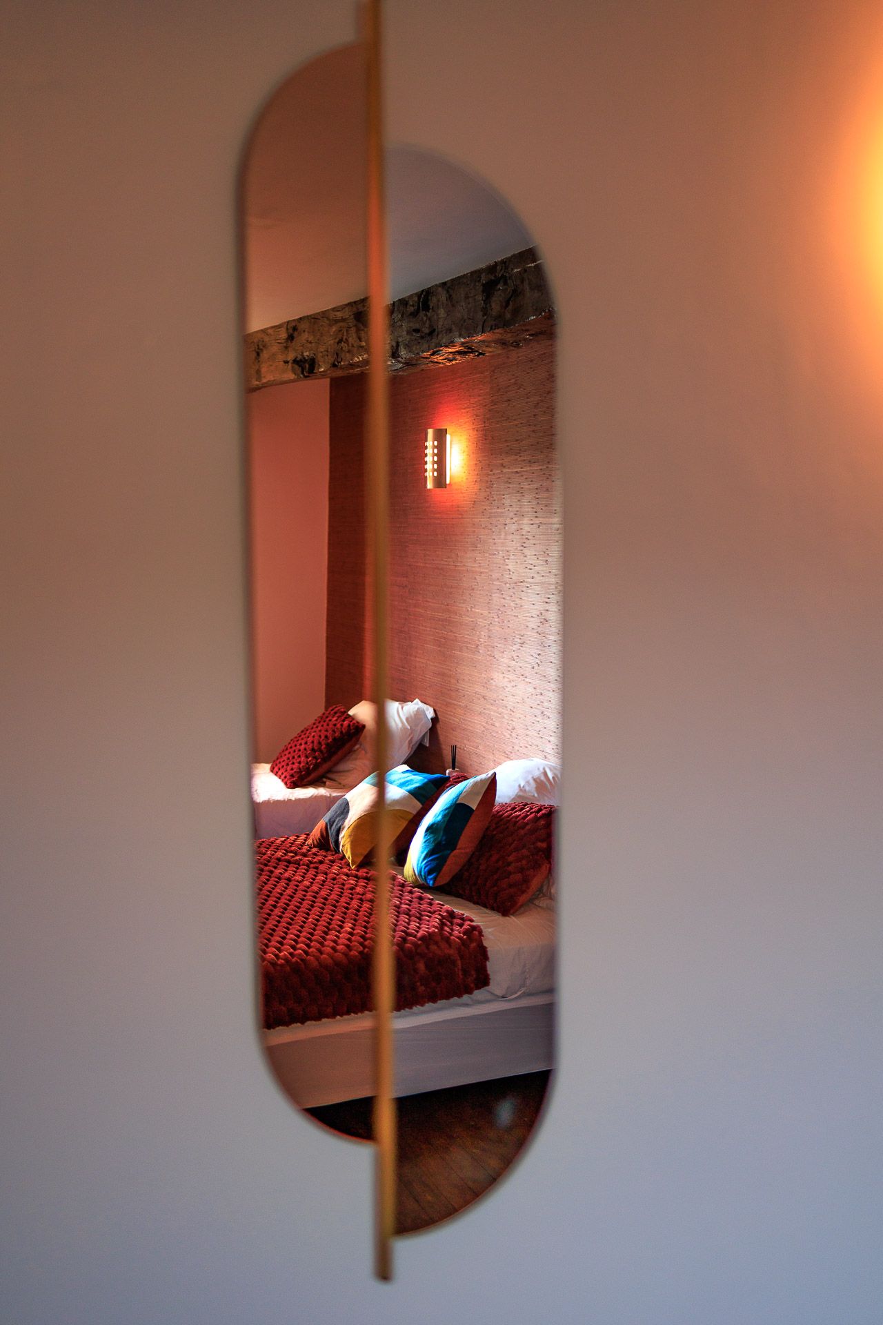 Reflet d'une parure de lit rouge et coussins colorés dans un miroir asymétrique