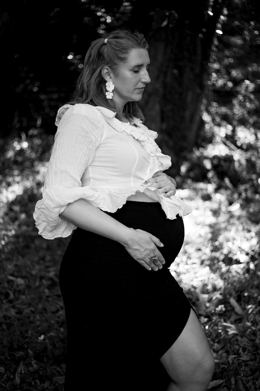 Portrait en noir et blanc d'une future maman élégante tenant son ventre en pleine nature.