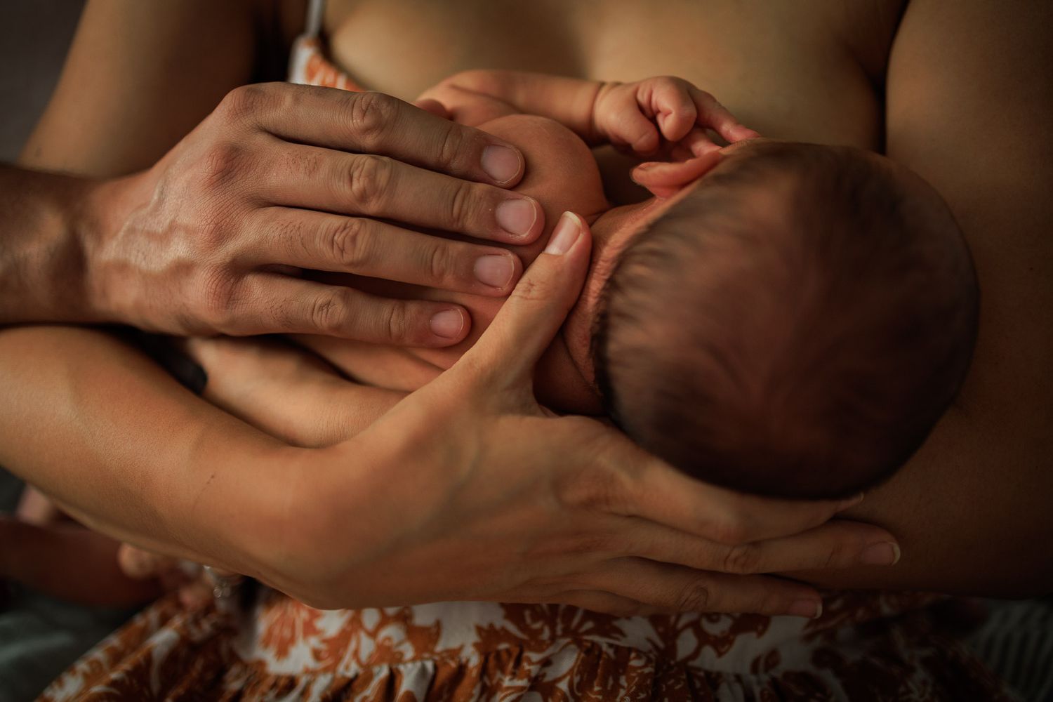 Les mains d'un papa et d'une maman posé sur le dos nu de leur nourrisson.