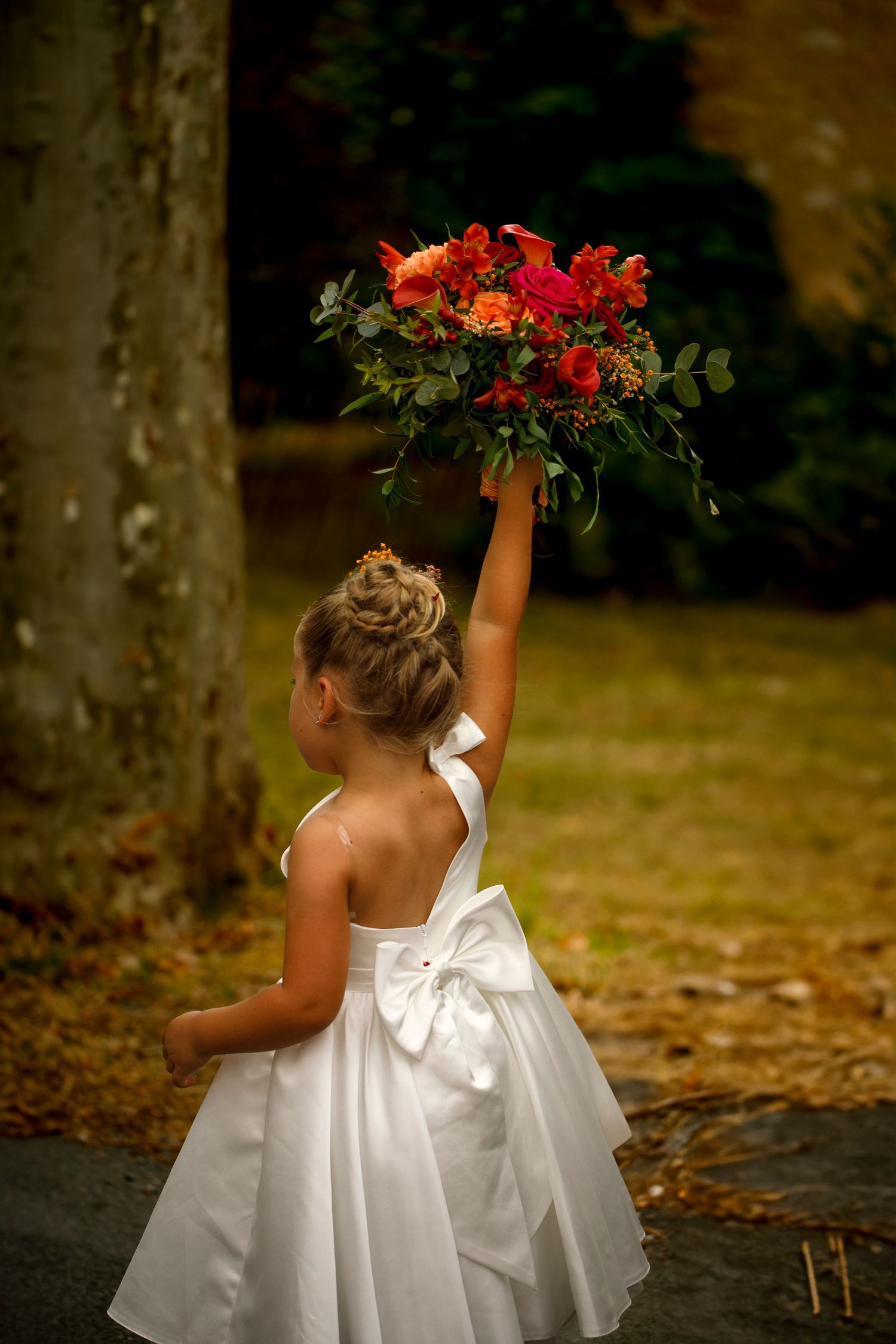 La fille des mariées brandit le bouquet de sa maman entre la mairie et l'église dans un village du Tarn