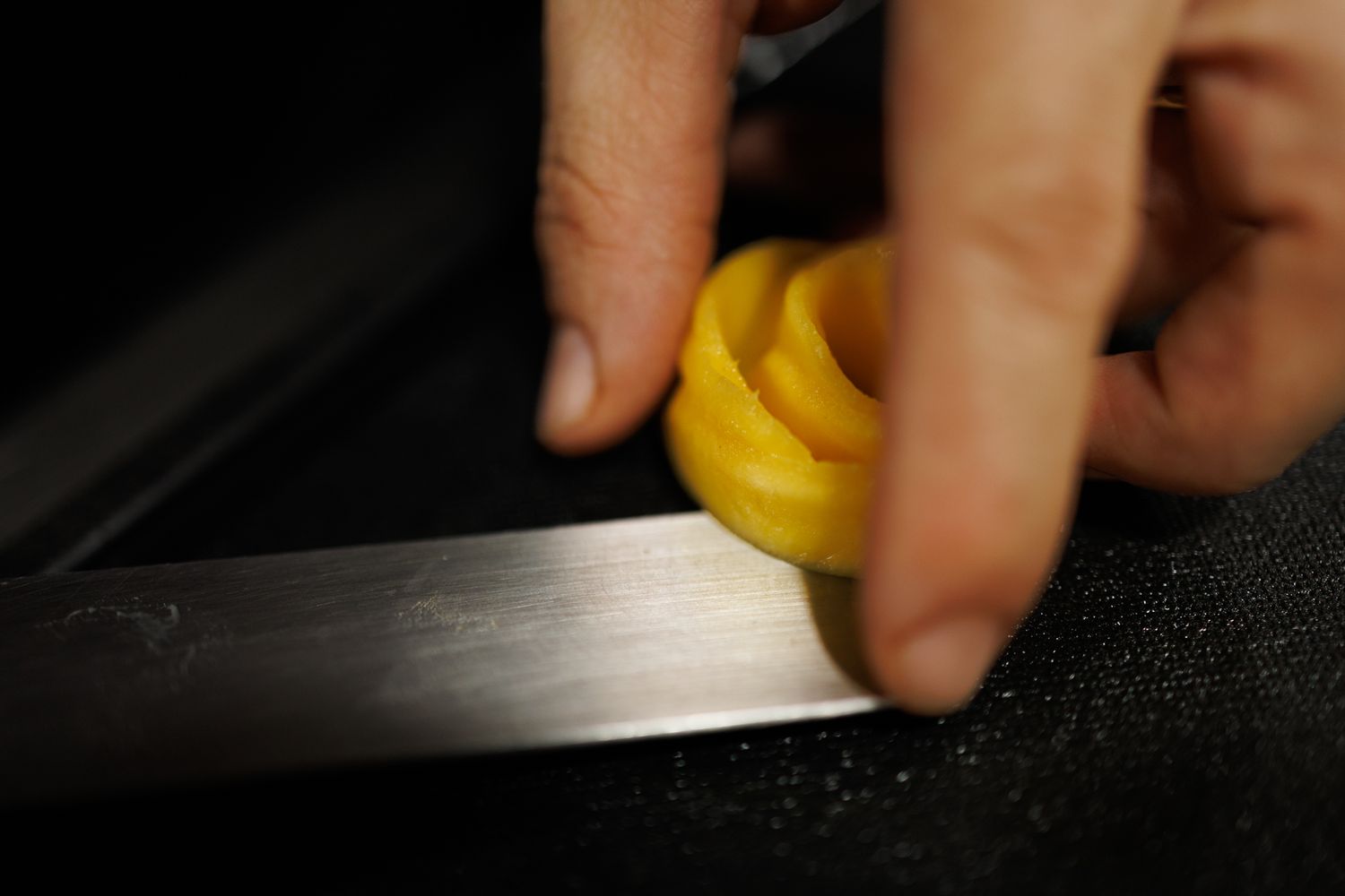 Gros plan sur la main de la cheffe pâtissière qui roule un fruit en guise de décoration pour sa pavlova plusieurs personnes.