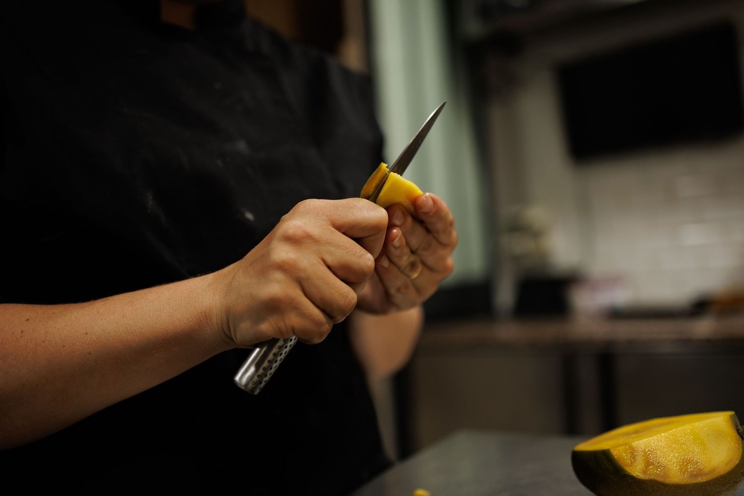 Les mains d'une pâtissière découpant pelant soigneusement une mangue au couteau.
