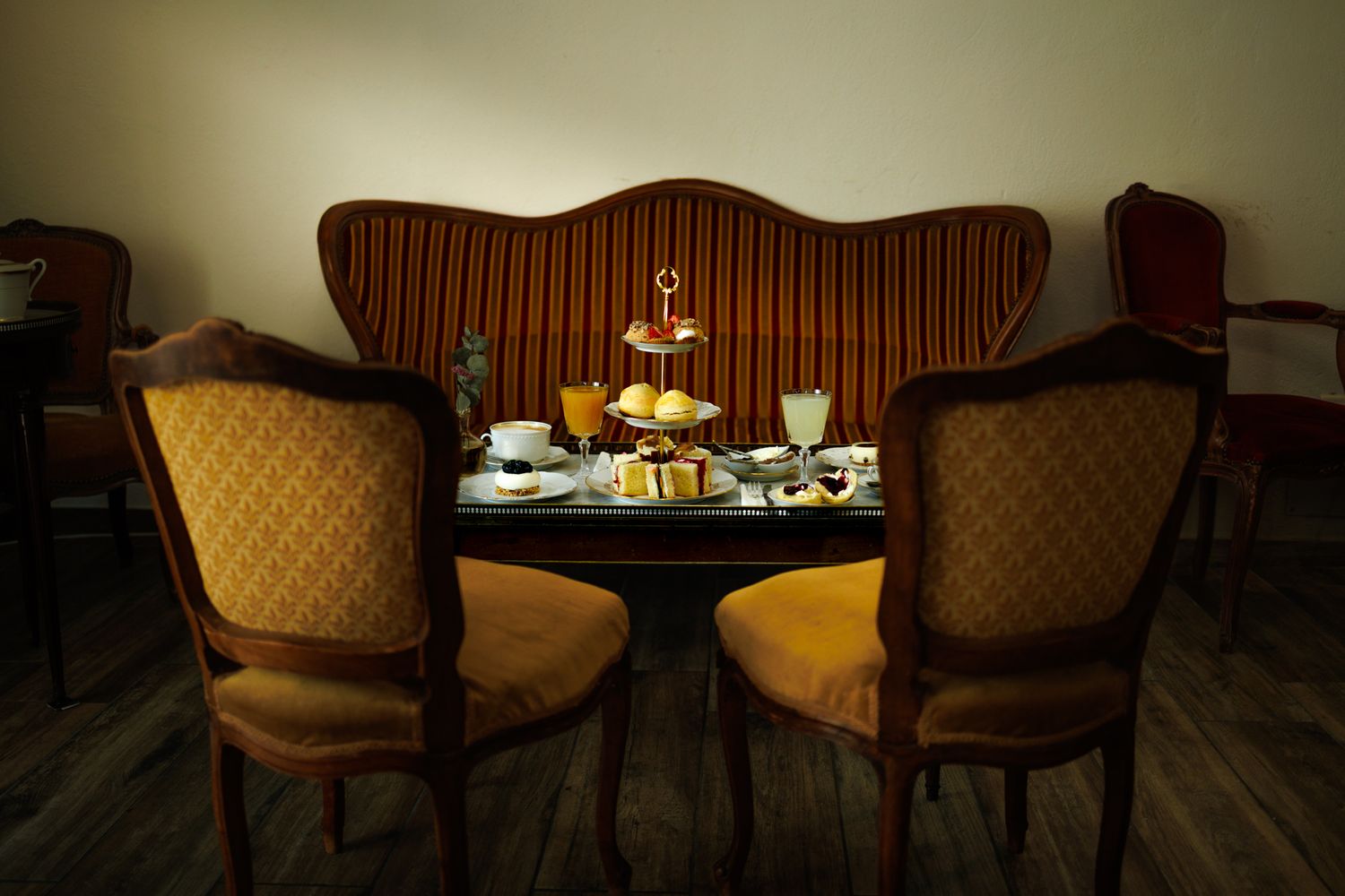 Table bouillotte rectangulaire encadrée par une banquette et des fauteuils Louis XV. Sur la table, un Tea Time à l'anglaise.