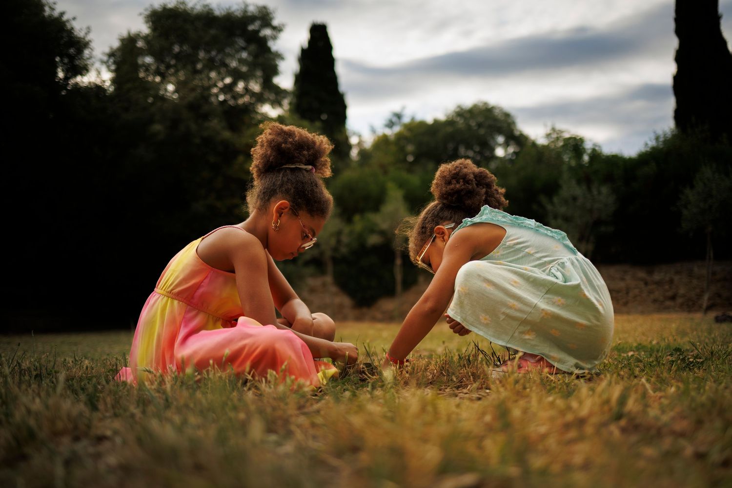 Deux petites filles jouent accroupies dans l'herbe.