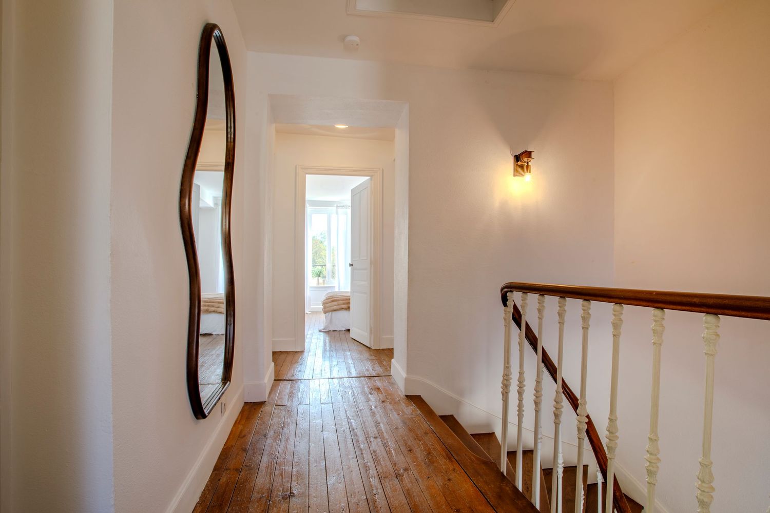 Couloir lumineux avec parquet ancien et miroir design menant aux chambres d'un domaine de prestige près de Mazamet.
