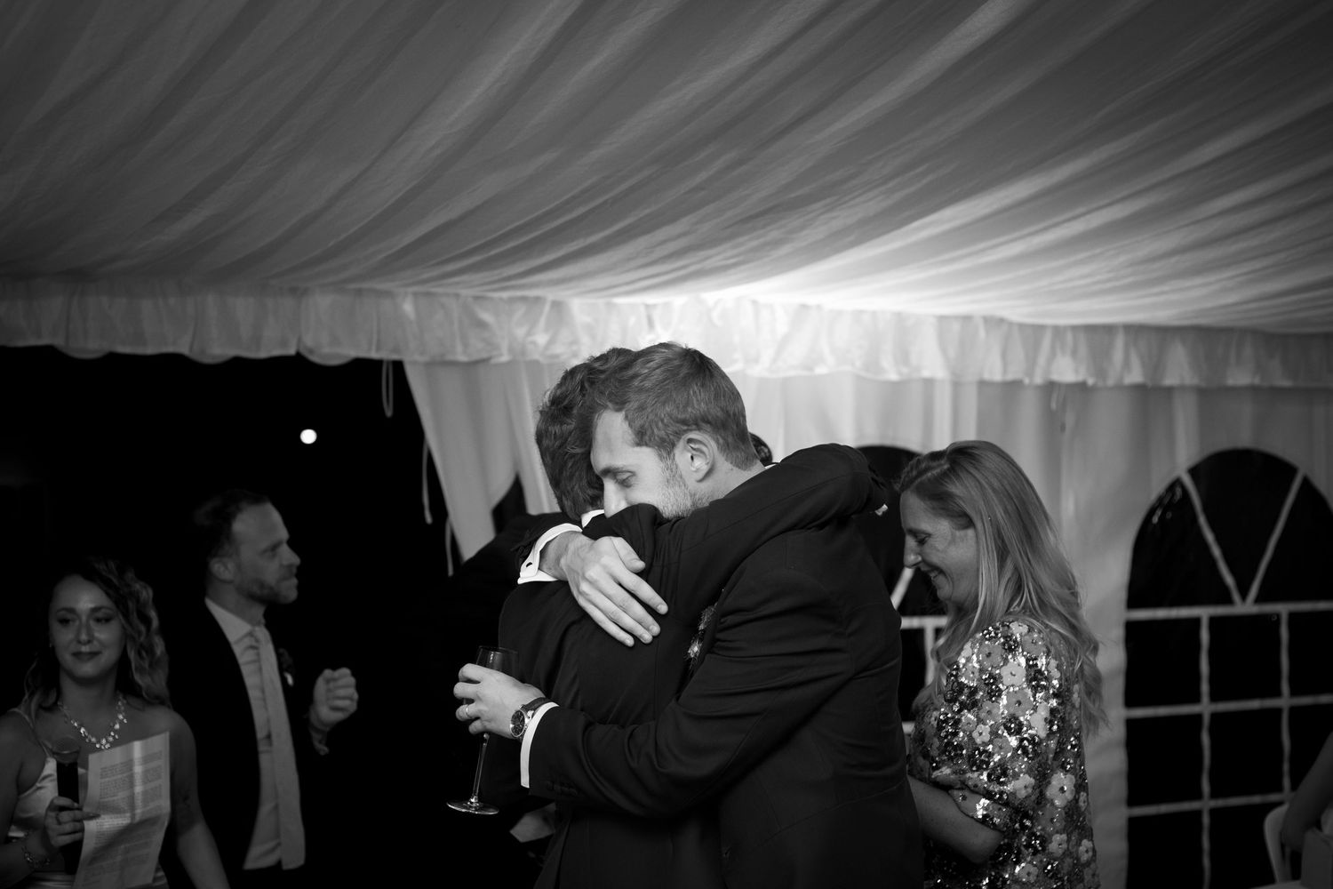 Reportage photo de mariage, photo noir et blanc, le marié enlace son frère après le discours