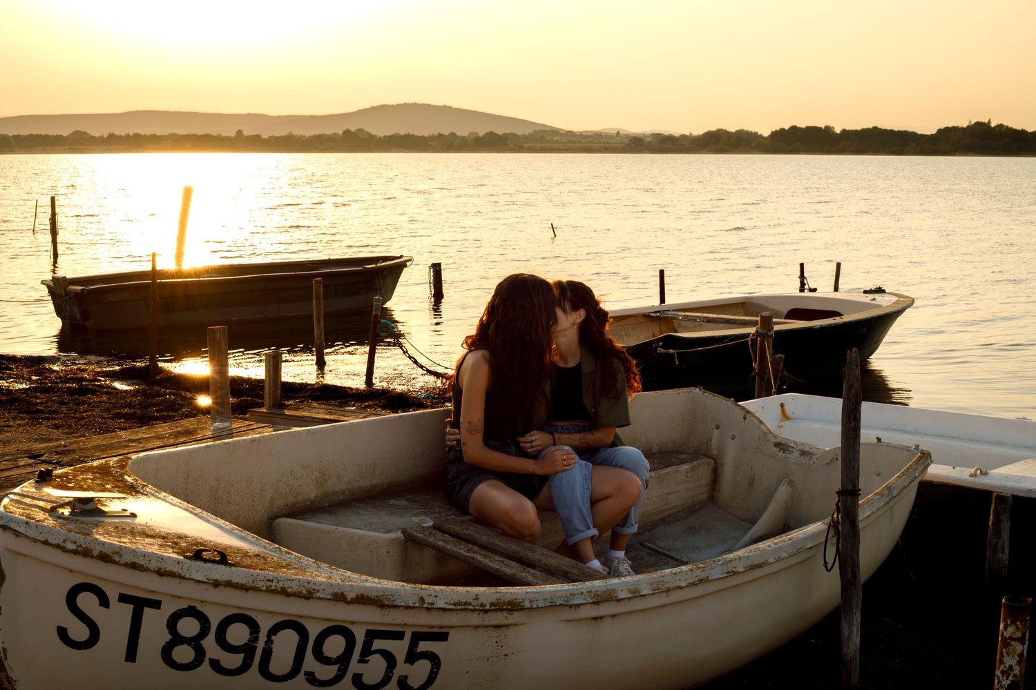 Photo d'un couple de femmes qui s'embrassent, assises dans une barque posée au bord de l'étang