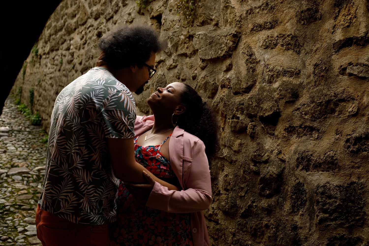 Photo d'un couple hétéro qui se regardent tendrement devant un mur de pierres