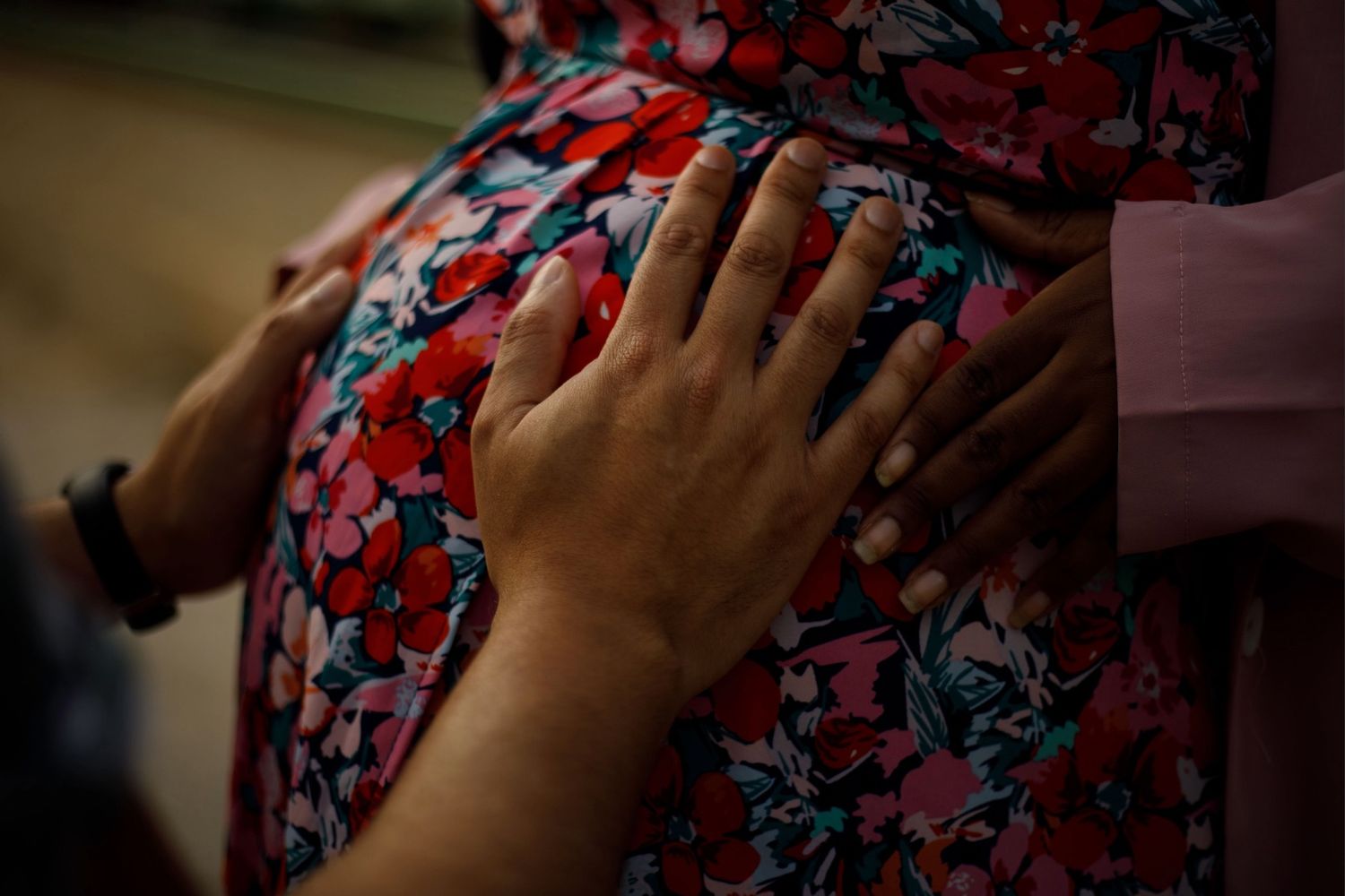 Mains des futurs parents posées sur le ventre rond de la maman en robe fleurie pendant un shooting grossesse