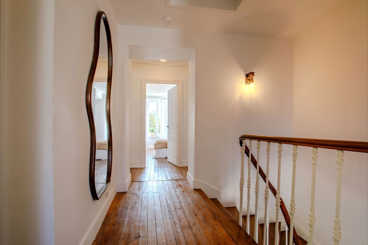 Couloir lumineux avec parquet ancien et miroir design menant aux chambres d'un domaine de prestige près de Mazamet.