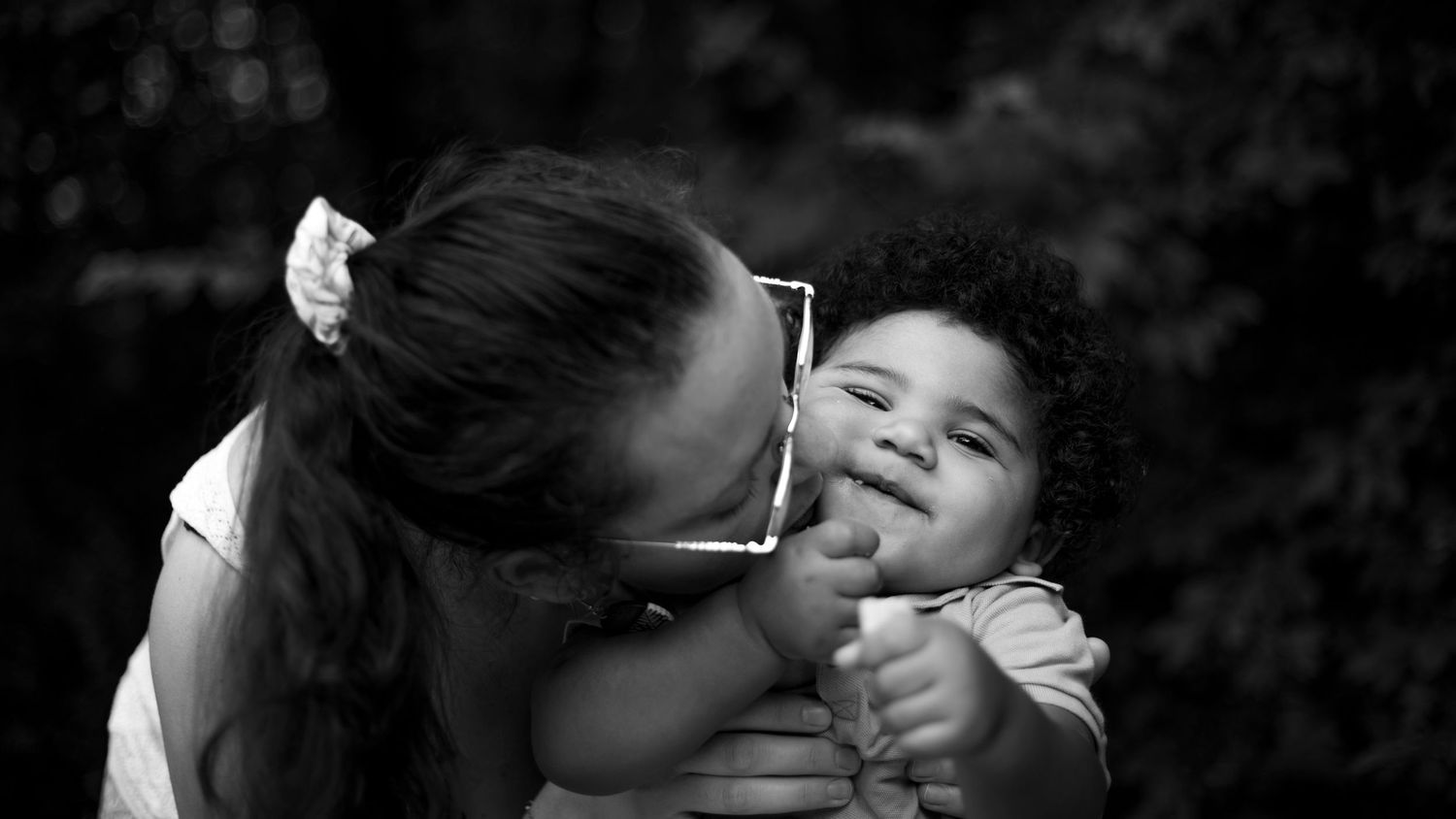 Photographie noir et blanc d'une maman qui embrasse pleinement son fils de un an sur la joue