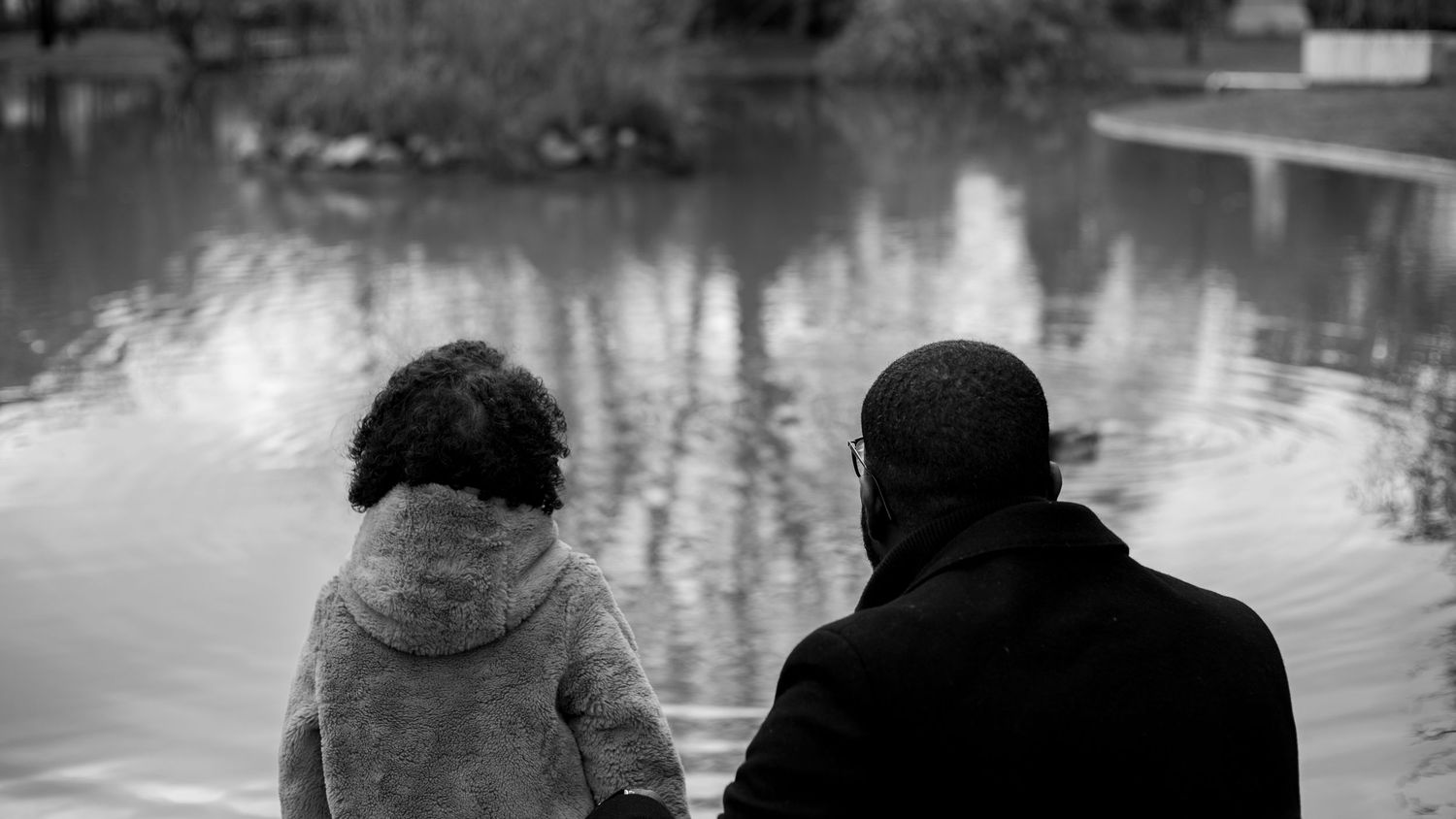 Photo noir et blanc un papa et sa fille de dos regardent ensemble dans la meme direction au bord de l'eau