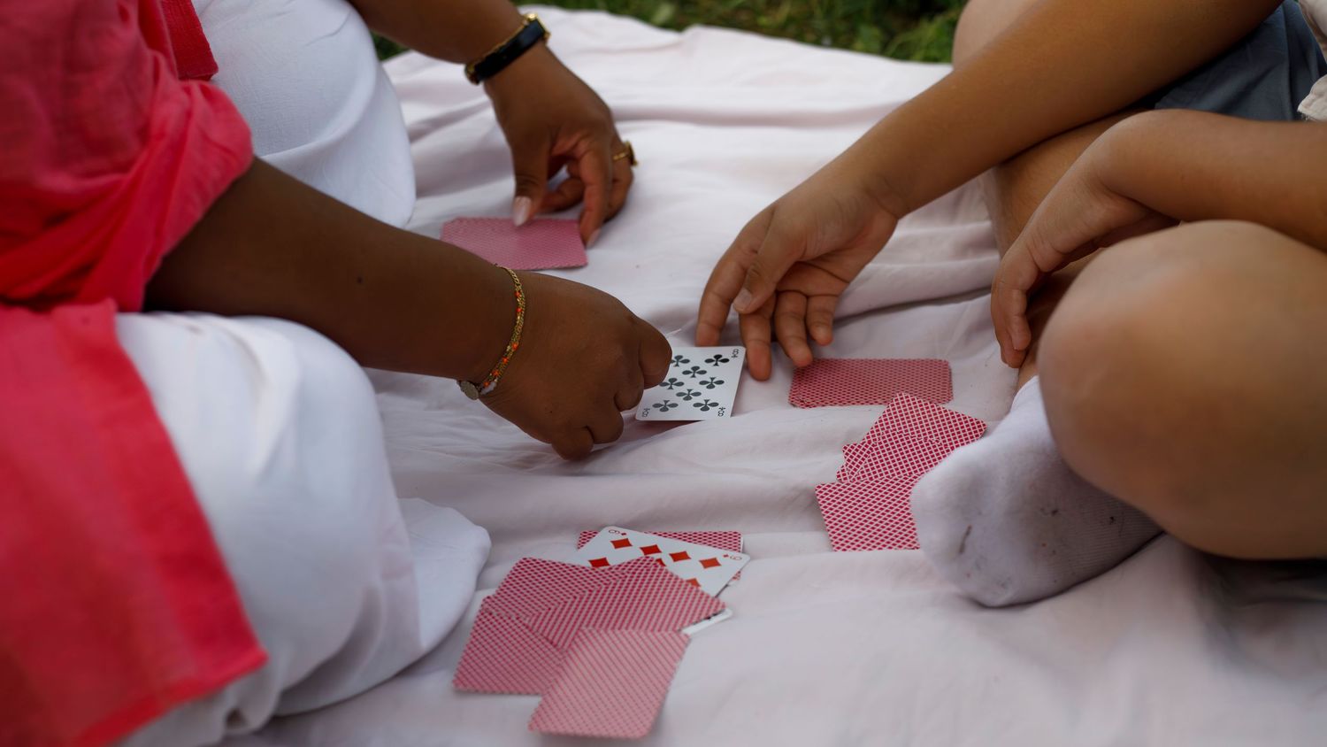 Des mains d'adulte et d'enfants jouent aux cartes sur une couverture de pique nique.