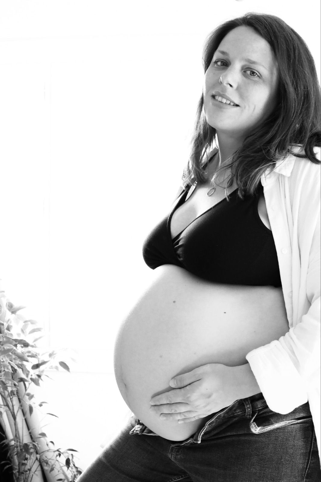 Portrait de femme enceinte souriante en noir et blanc sur fond clair lors d'une séance photo maternité