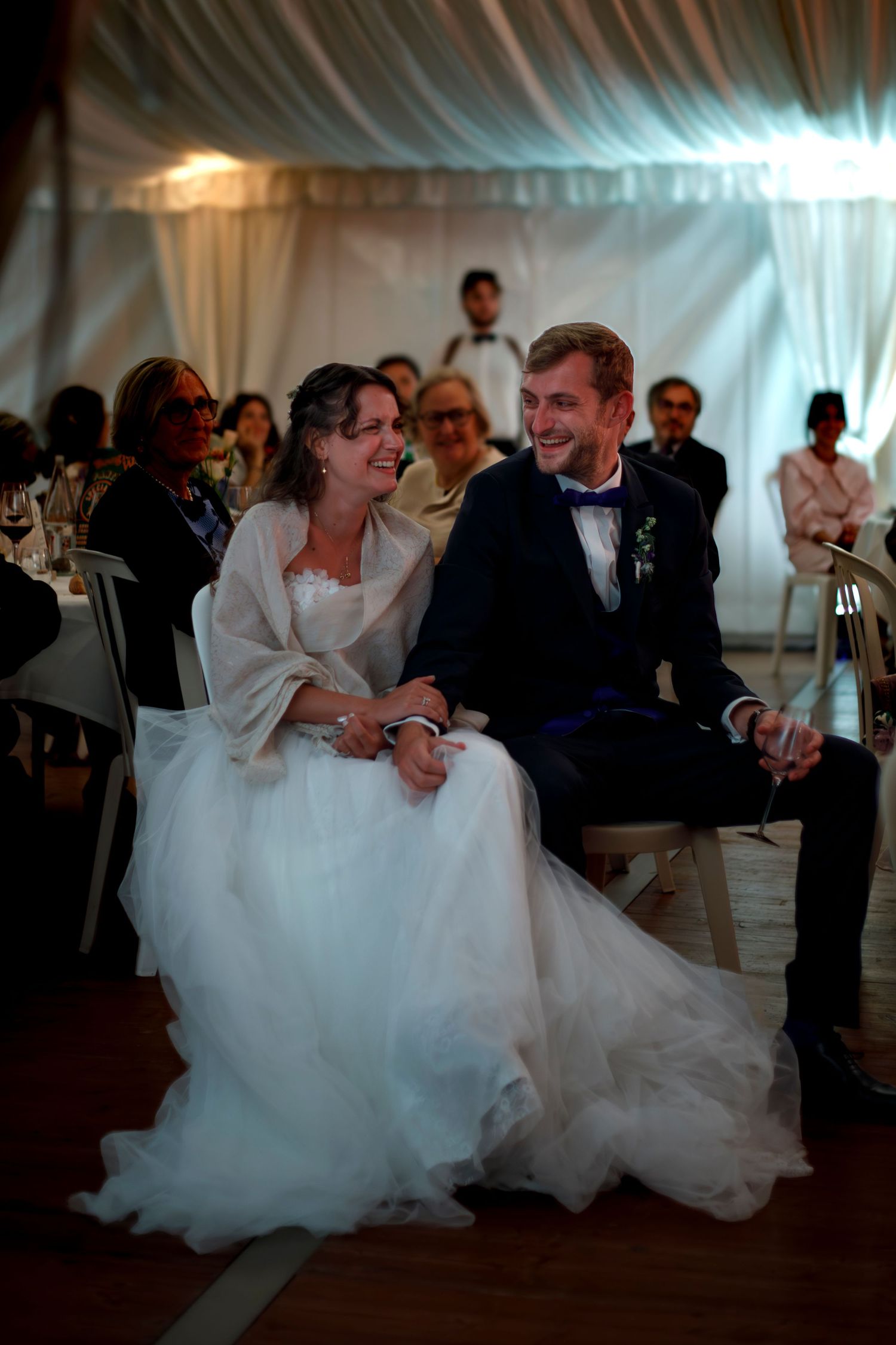 Photo d'un couple de mariés qui se regardent souriants lors d'un discours des témoins pendant un reportage photo de mariage