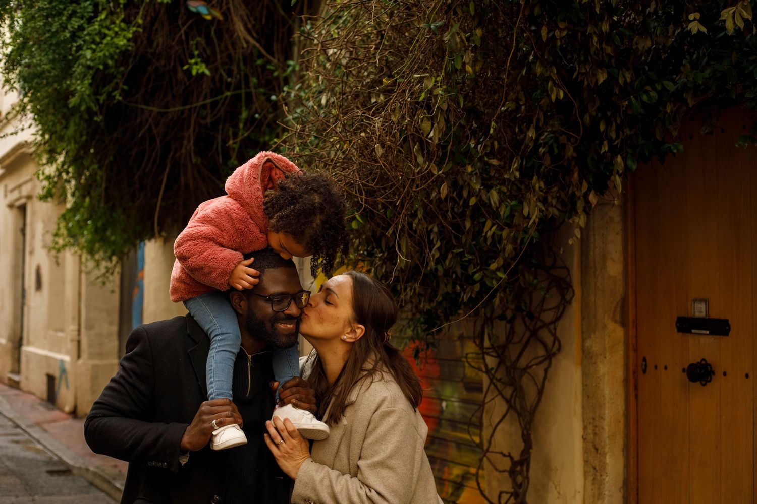 Photographie d'une famille dans l'écusson à Montpellier. La fille sur les épaules du père lui faisant un bisou et la maman aussi.