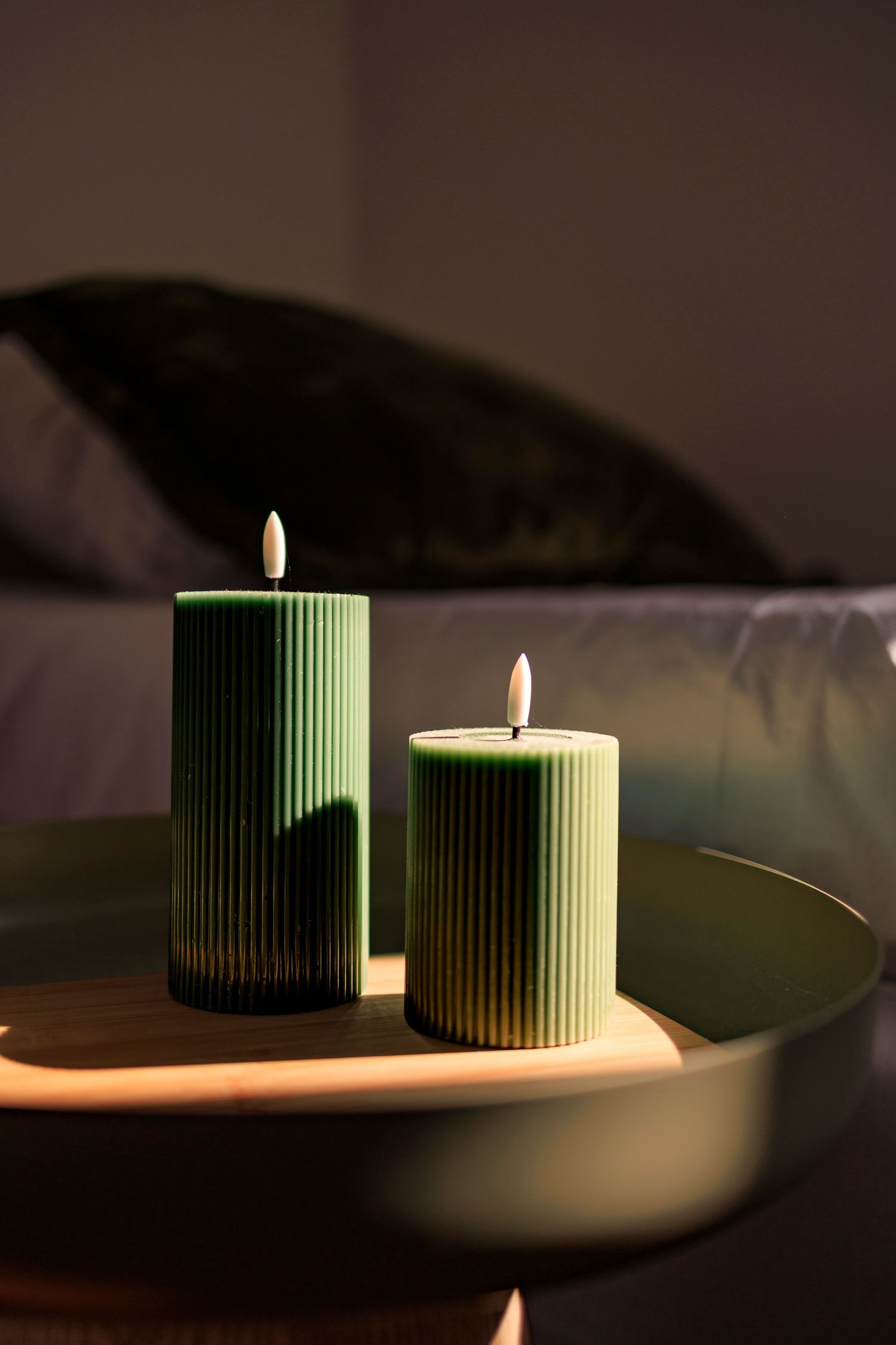 Deux bougies cannelées de couleur sauge éclairées par le soleil couchant dans une chambre d'un gîte de charme près de Castres.