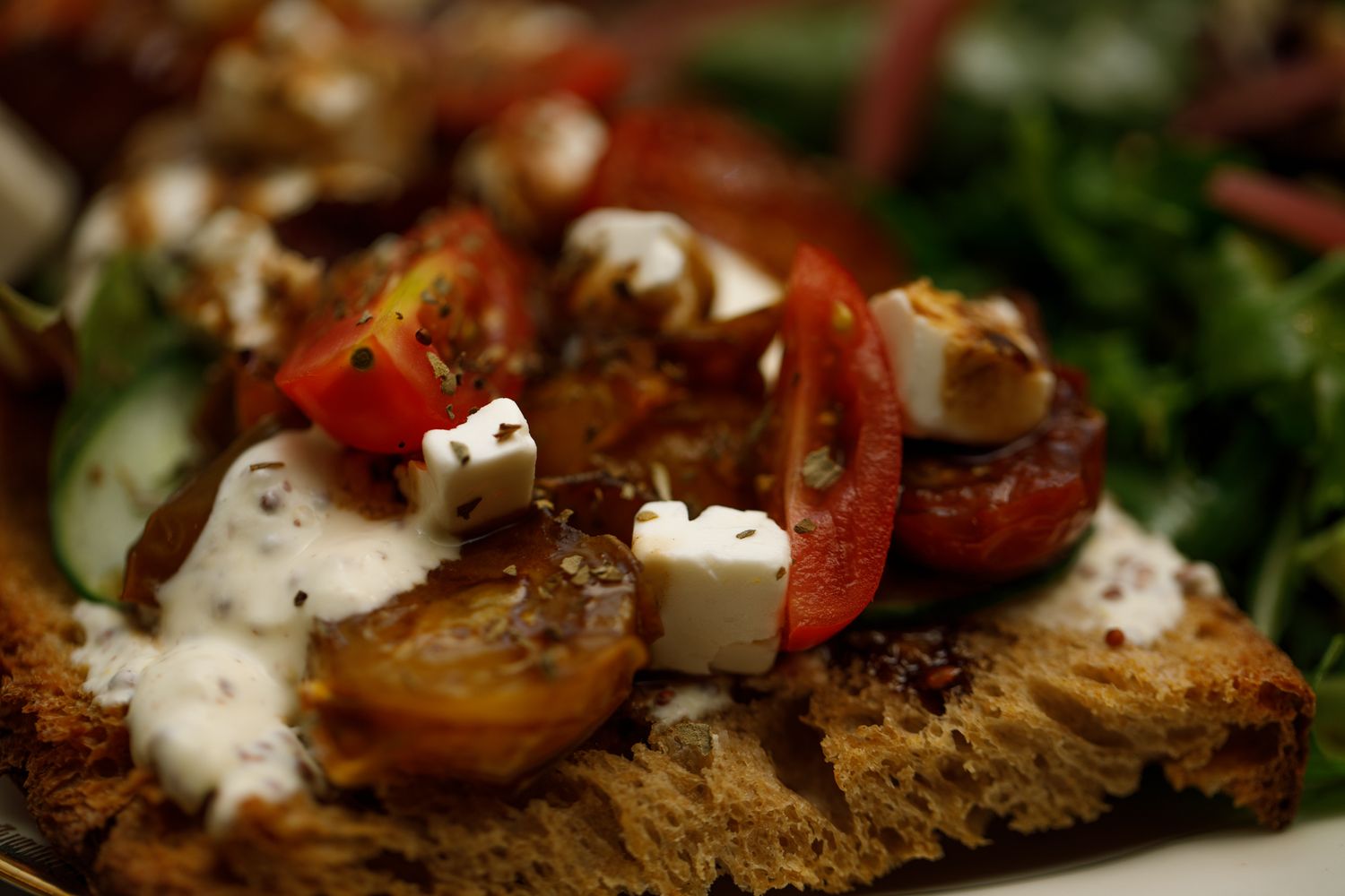 Plan macro sur une tartine de pain grillé agrémenté de carrés de fêta, tomates cerise coupées, vinaigre balsamique et salade