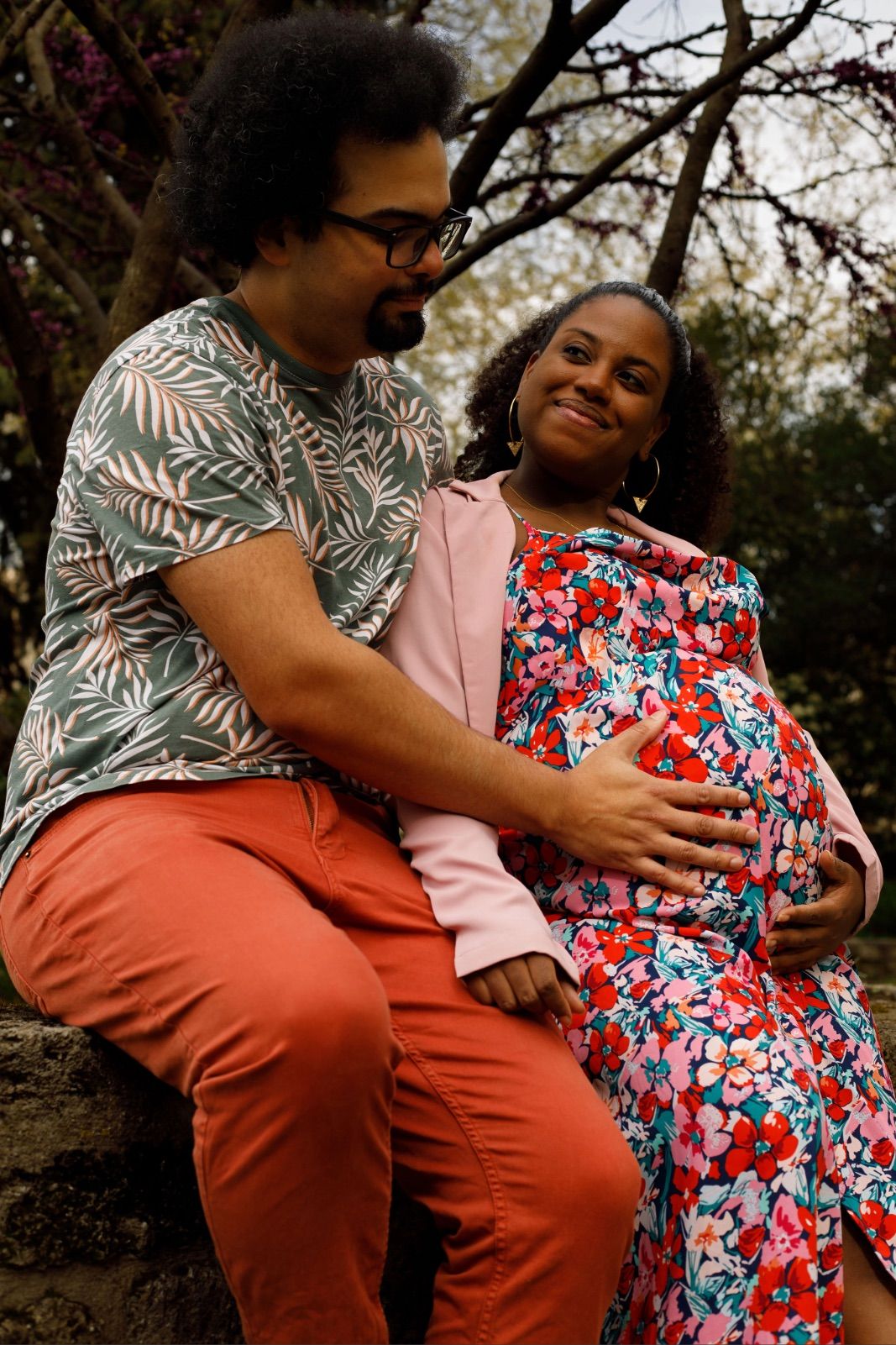 Futur papa et future maman assis en extérieur et souriants pendant leur séance photo couple et grossesse.