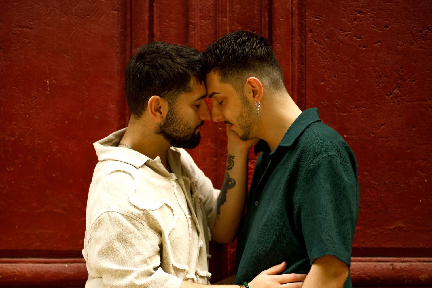 Deux hommes front contre front, yeux fermés devant une porte rouge.