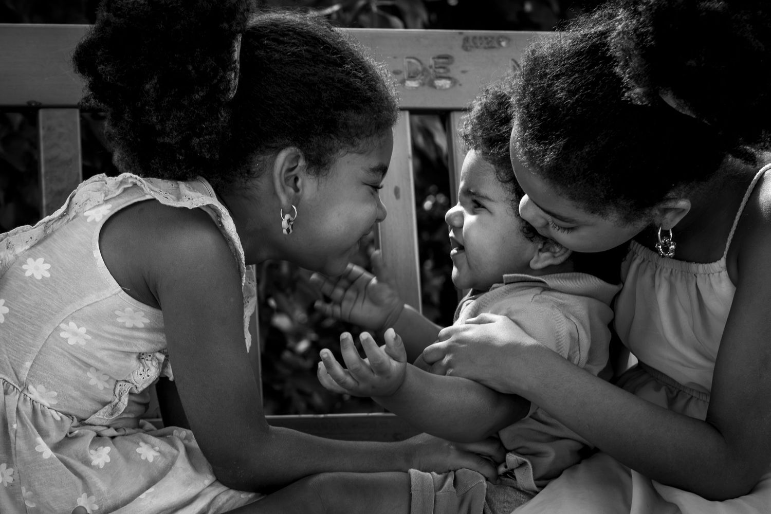 Photographie noir et blanc de trois enfants d'âges différent qui se chatouillent.