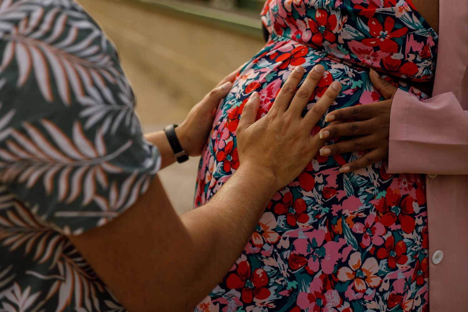 Les mains du futur papa posé sur le ventre rond de sa compagne en robe à fleurs.