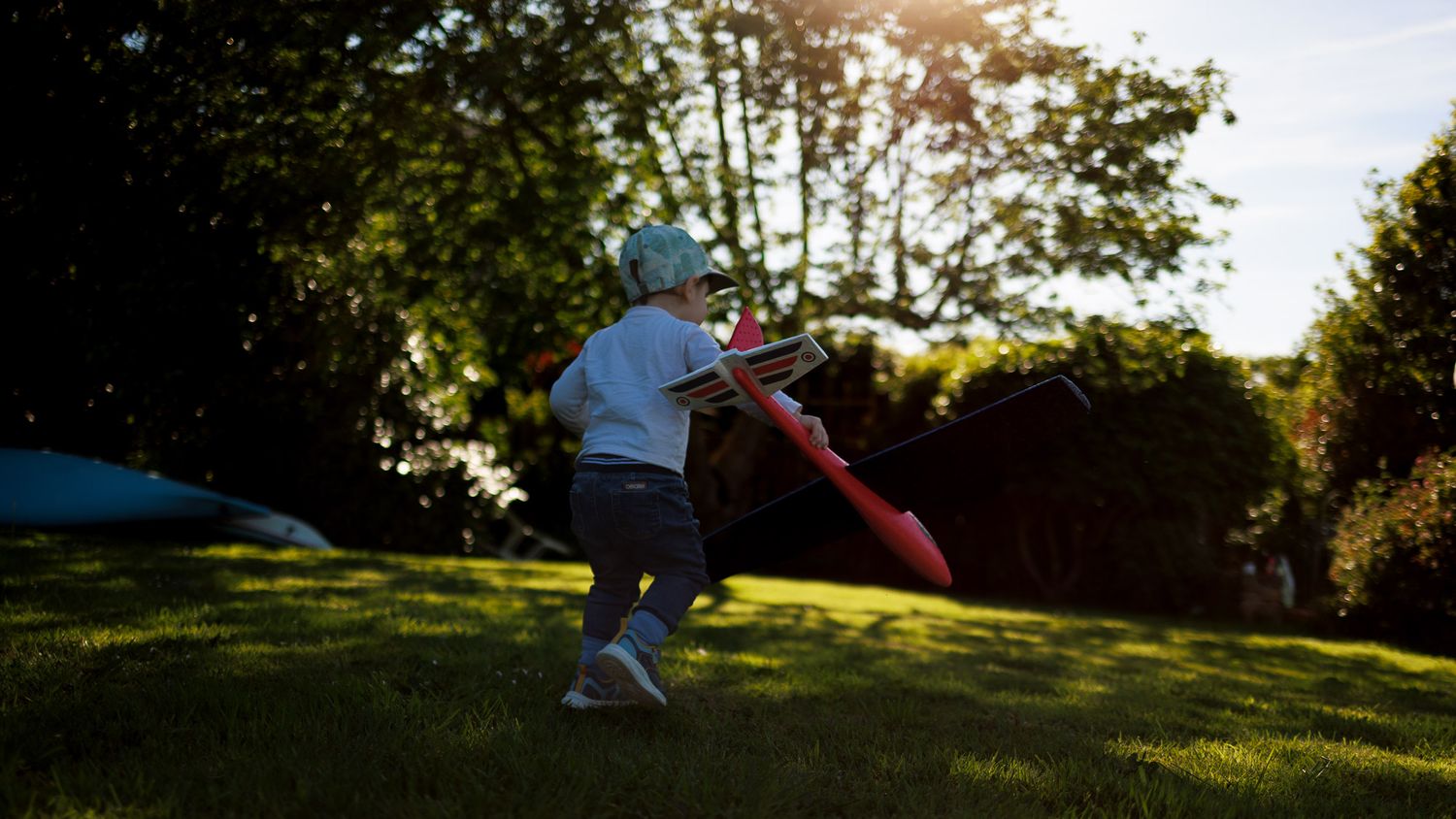 Un jeune enfant court sur une pelouse avec un avion rouge dans la main à contre-jour.