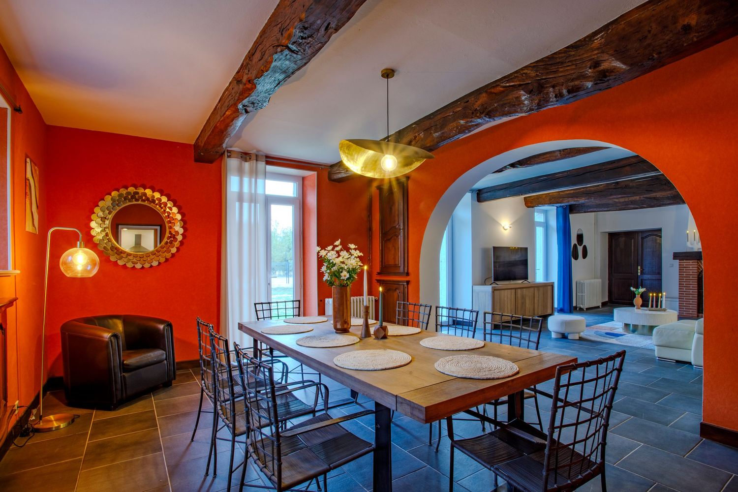 Salle à manger et espace de vie spacieux dans un domaine de prestige près de Mazamet avec des murs orange audacieux, des poutres apparentes.