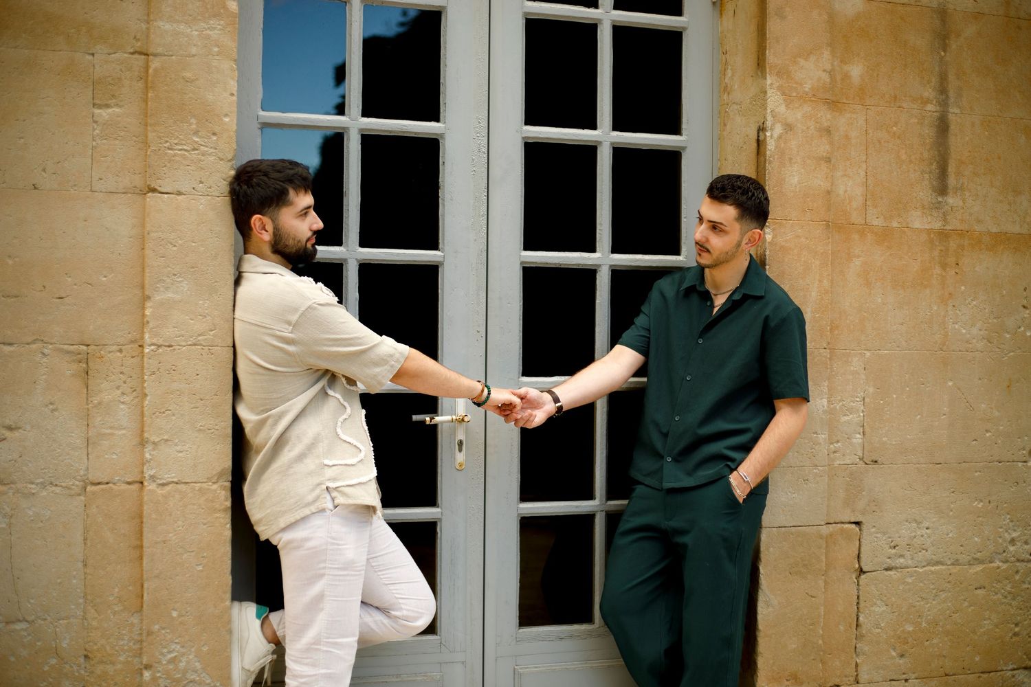 Photo d'un couple d'homme appuyés sur l'encadrement d'une fenêtre ils se tiennent la main et se regardent tendrement