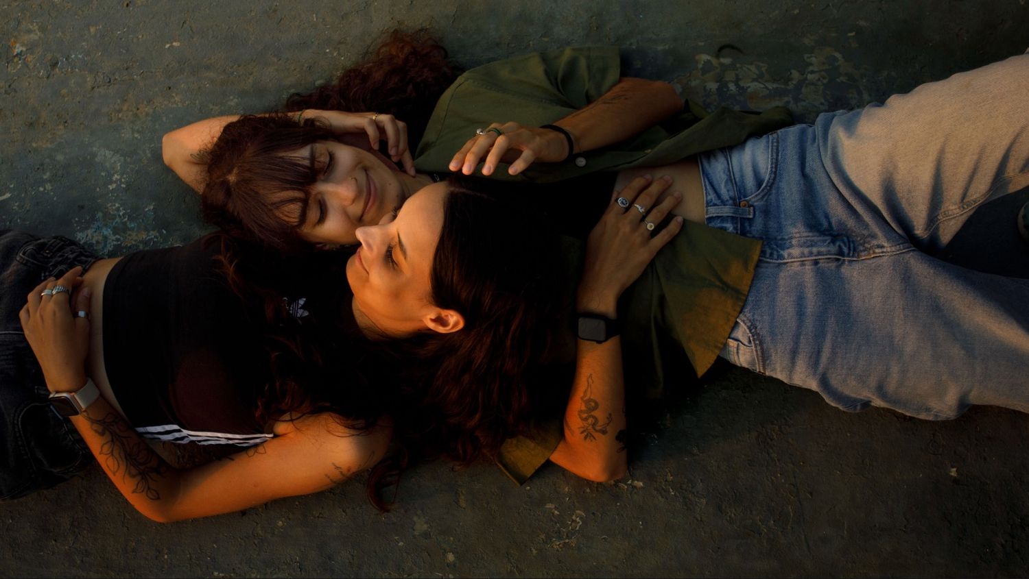 Photo d'un couple de femmes allongées la tête sur l'épaule l'une de l'autre, les mains dans les cheveux.