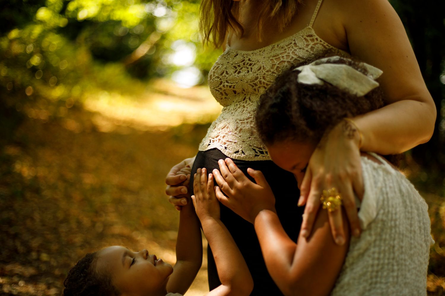 Deux petites filles posent tendrement leurs mains sur le ventre rond de leur maman enceinte en extérieur