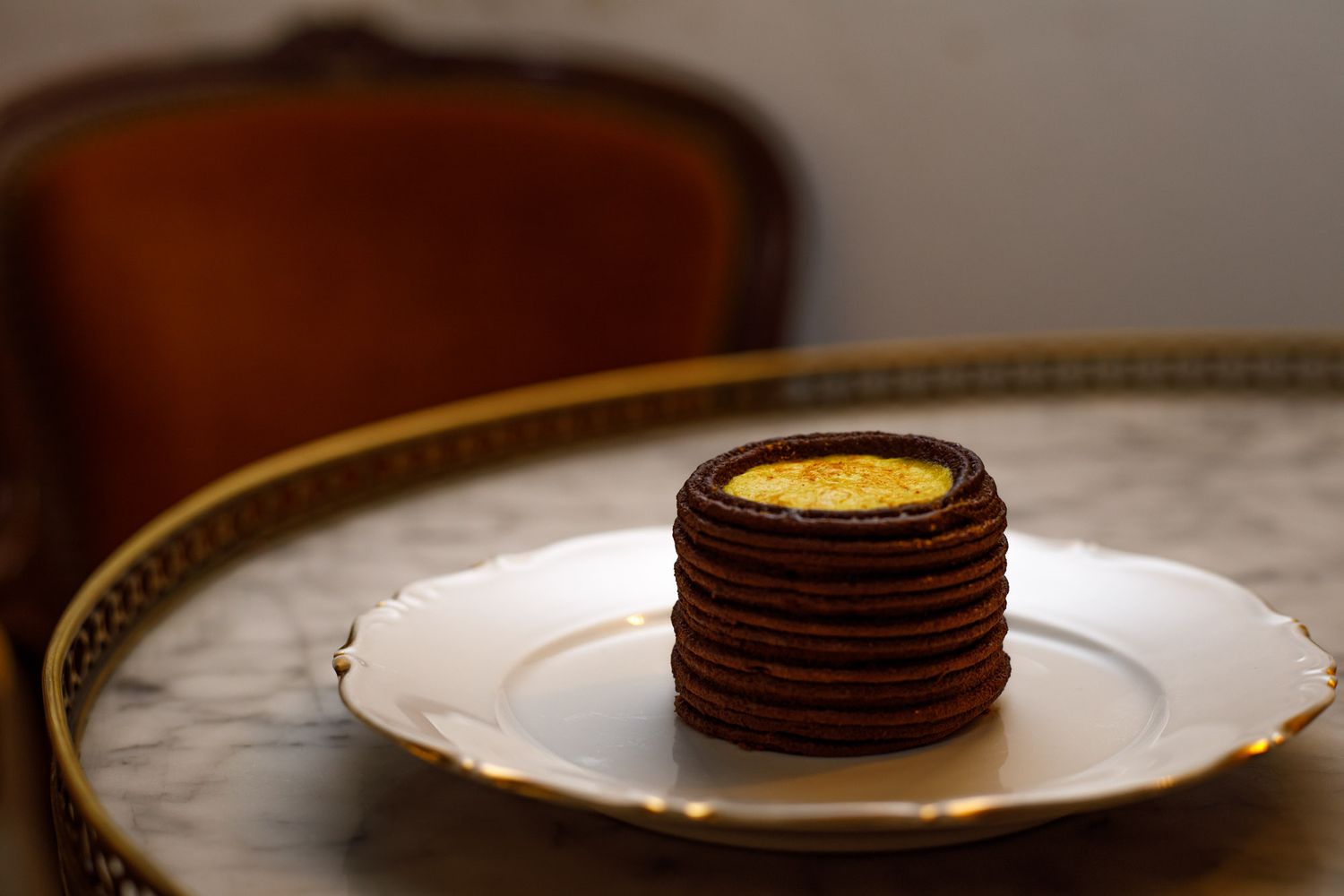 Entremet au chocolat et lait d'or déposé sur une assiette en porcelaine, elle meme sur une table bouillotte en marbre
