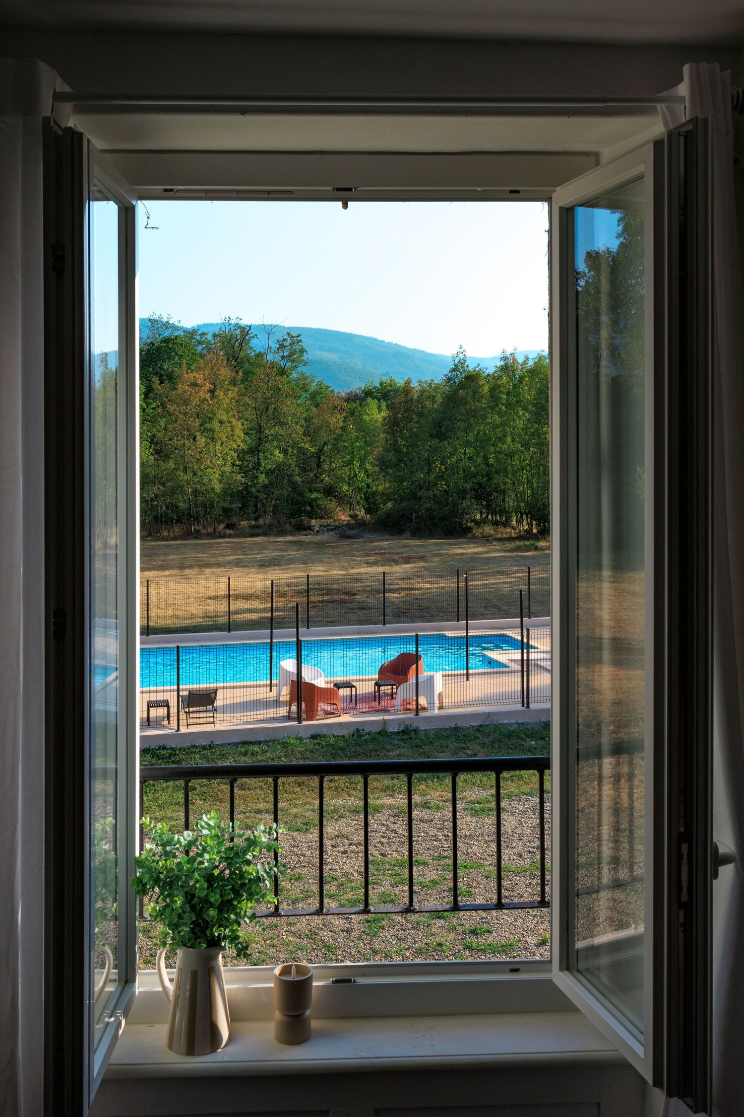 Vue depuis l'intérieur d'une chambre à travers une fenêtre ouverte sur une piscine sécurisée et vue sur la Montagne Noire