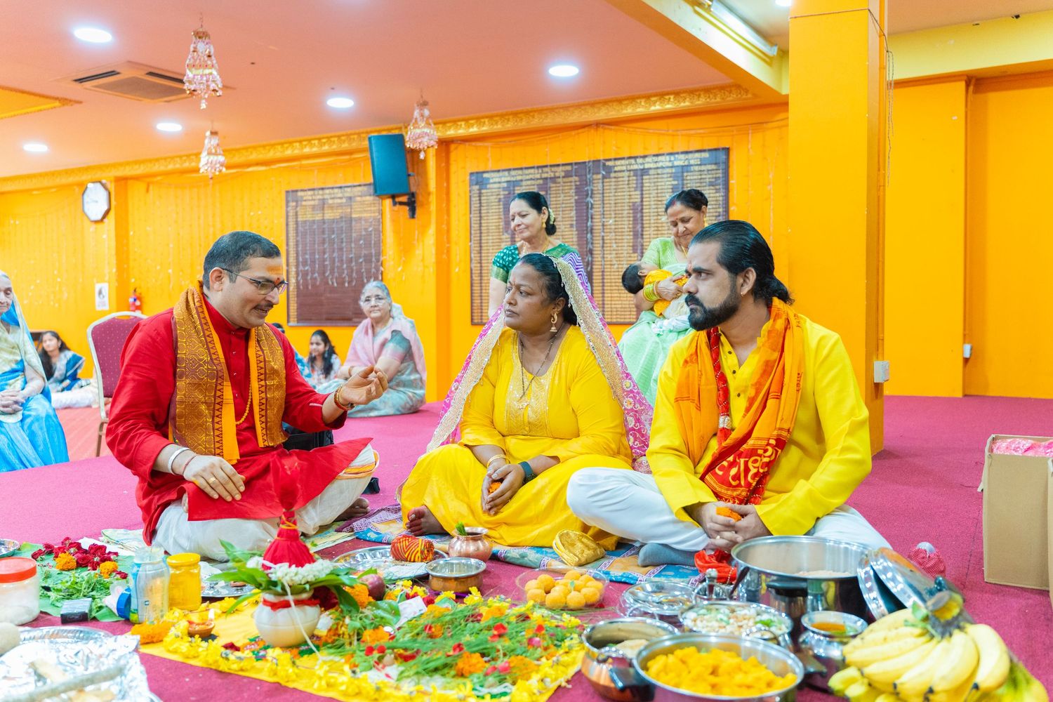 Hindu priest performing traditional puja ceremony with devotees in yellow attire at a colorful temple.