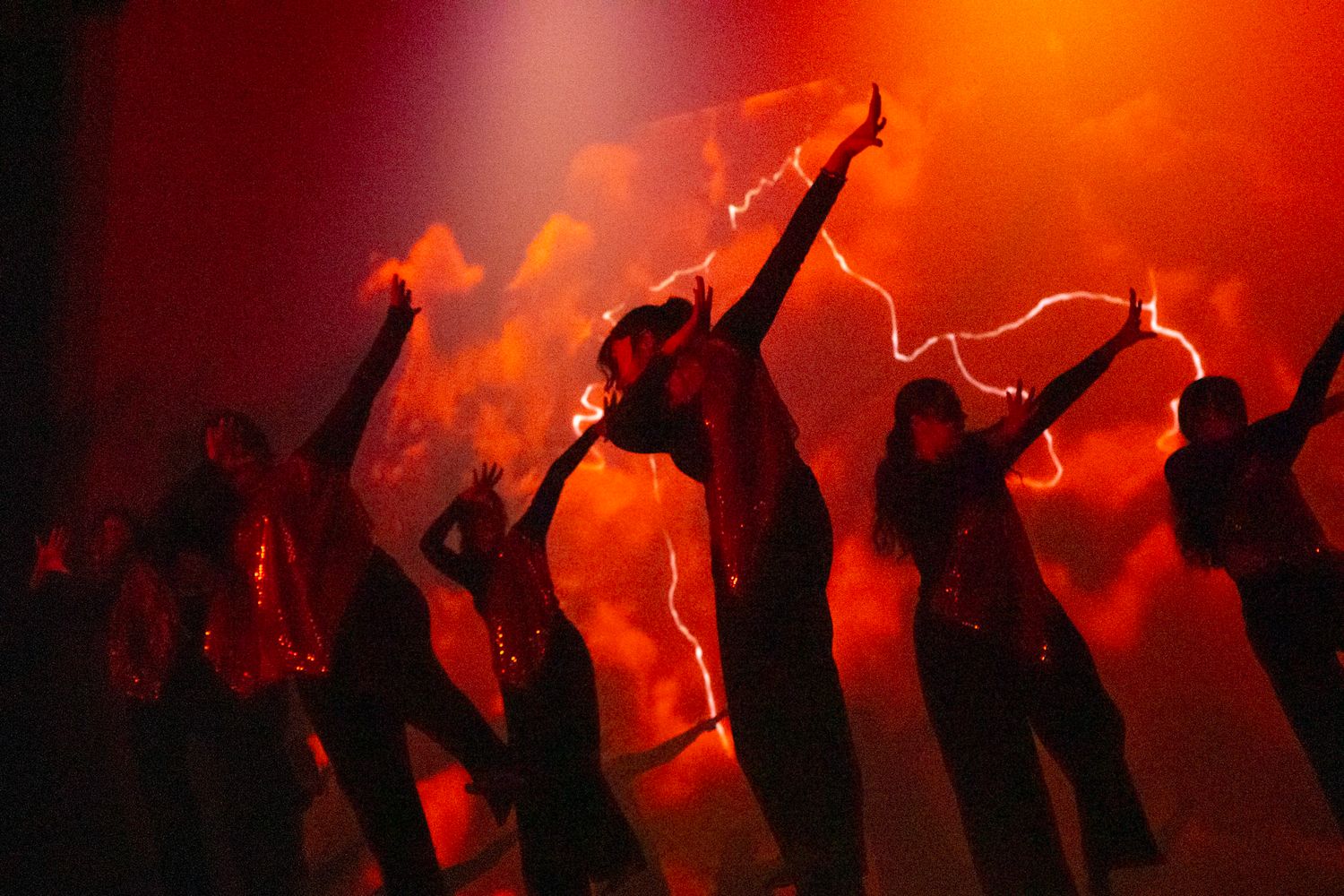 Silhouettes of dancers performing against a vibrant red-orange backdrop with dramatic lighting effects.